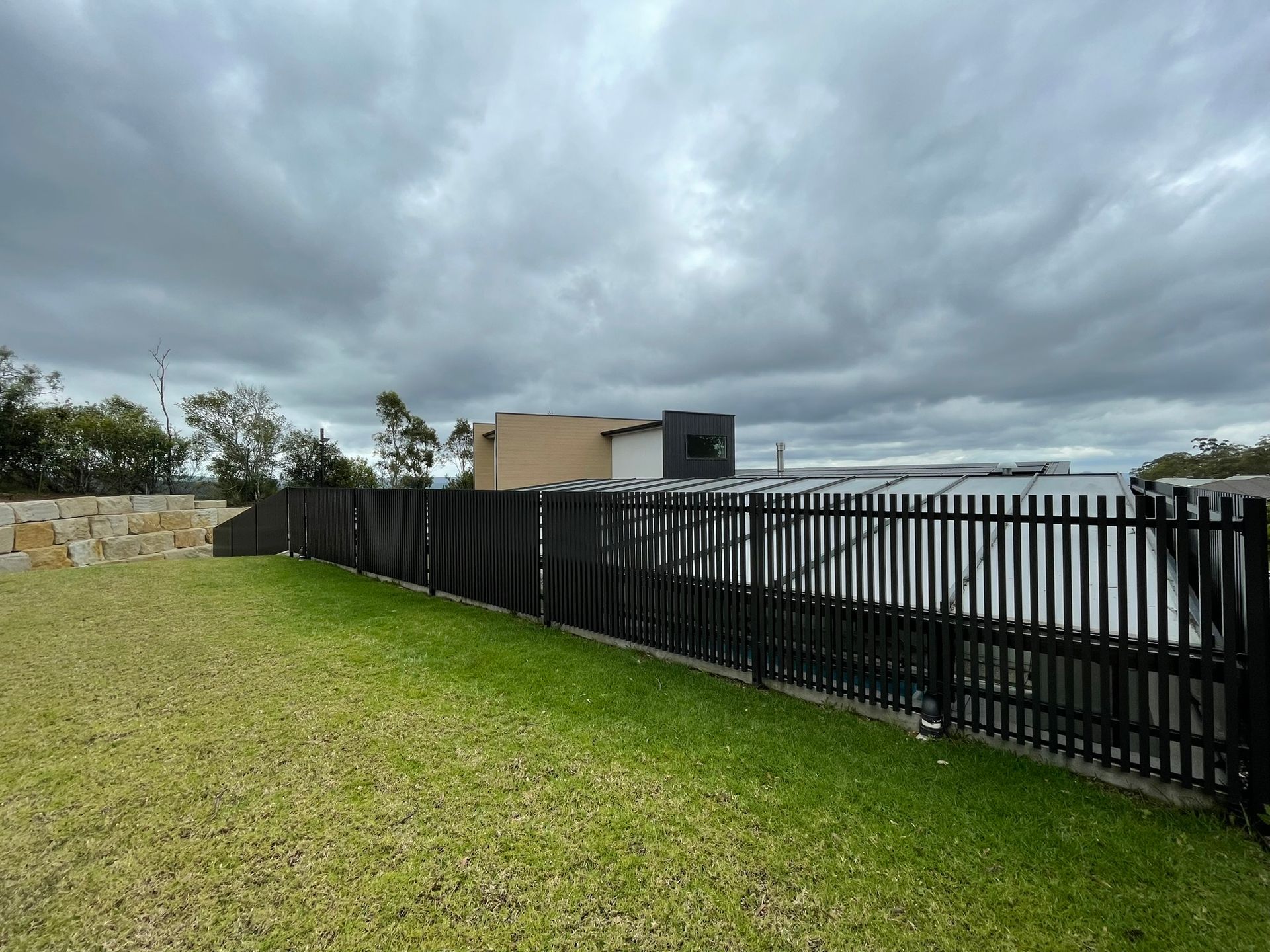 A black fence surrounds a lush green field with a cloudy sky in the background.