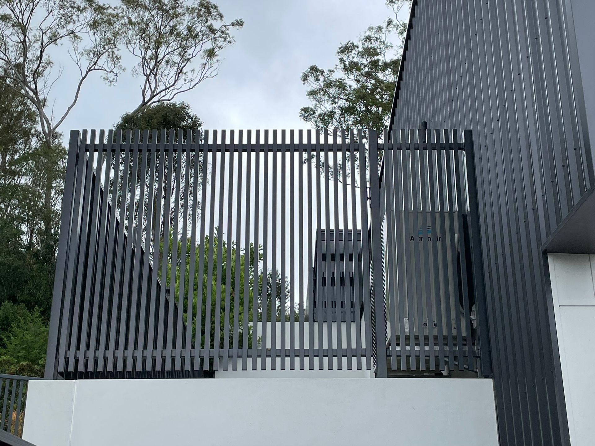 A black fence is sitting on top of a white wall next to a building.