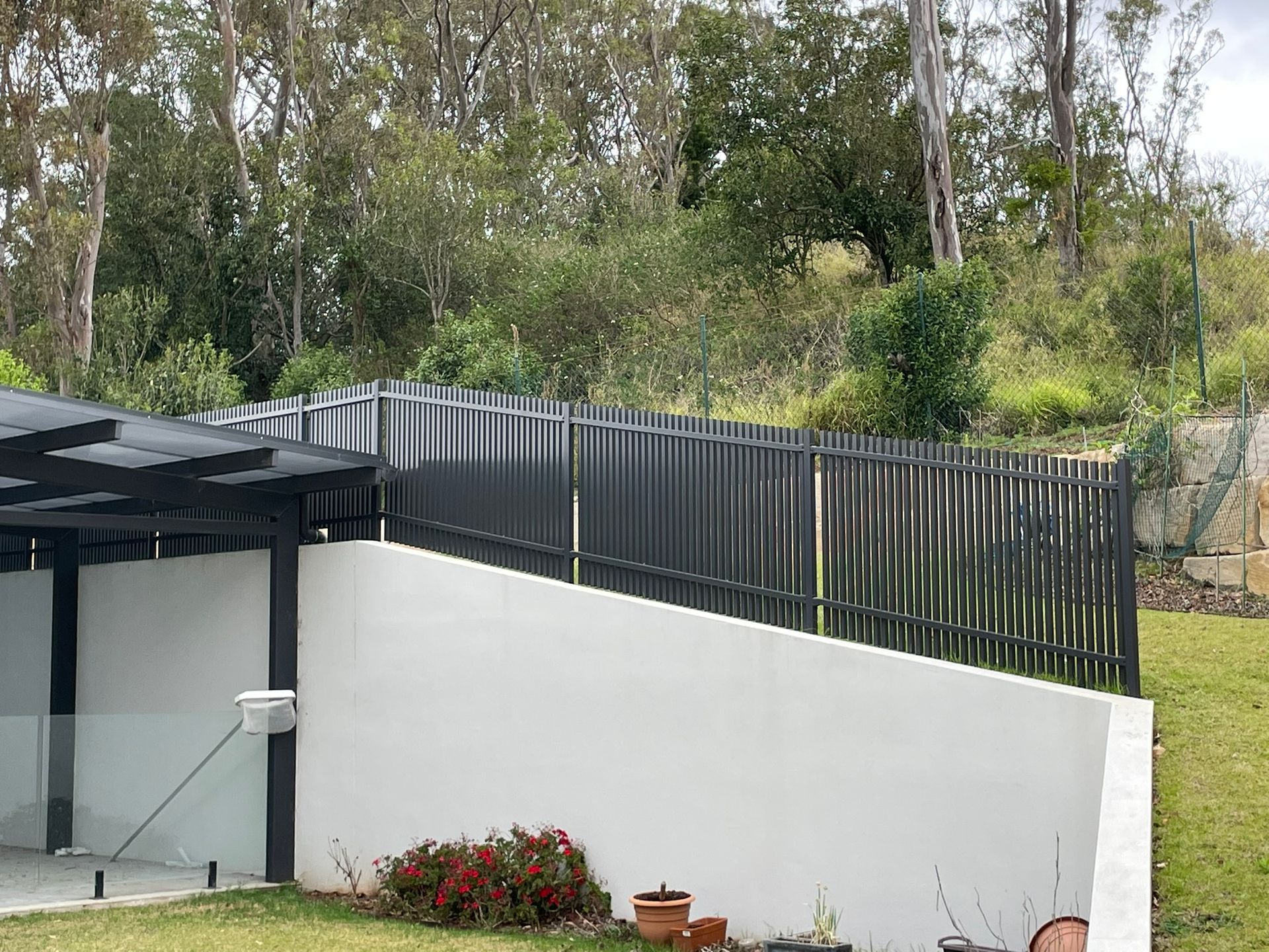 A black fence is surrounding a white wall in a yard.