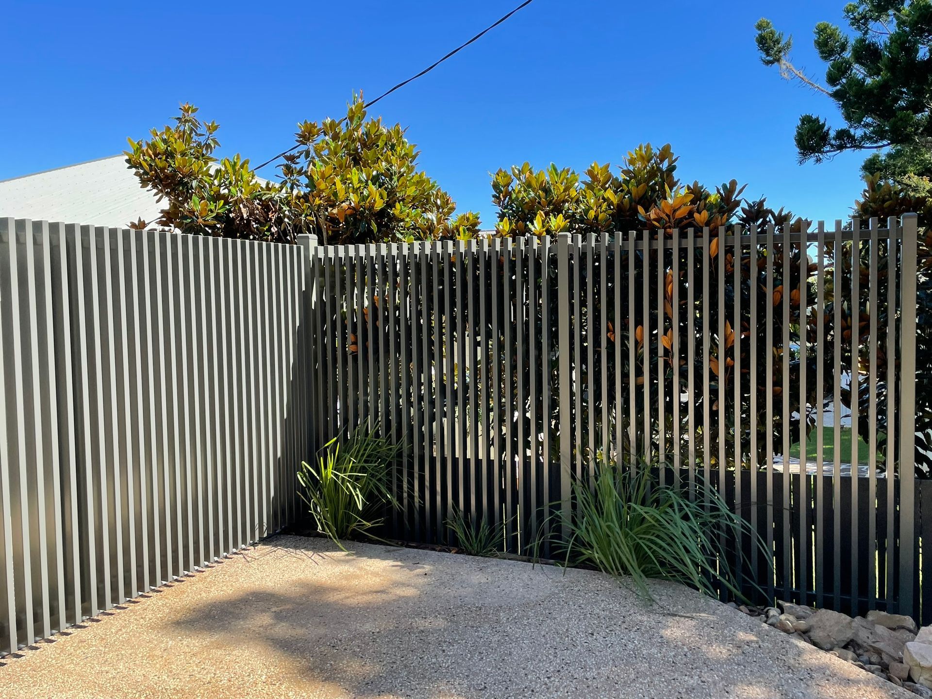 A fence is surrounding a gravel driveway with trees in the background.