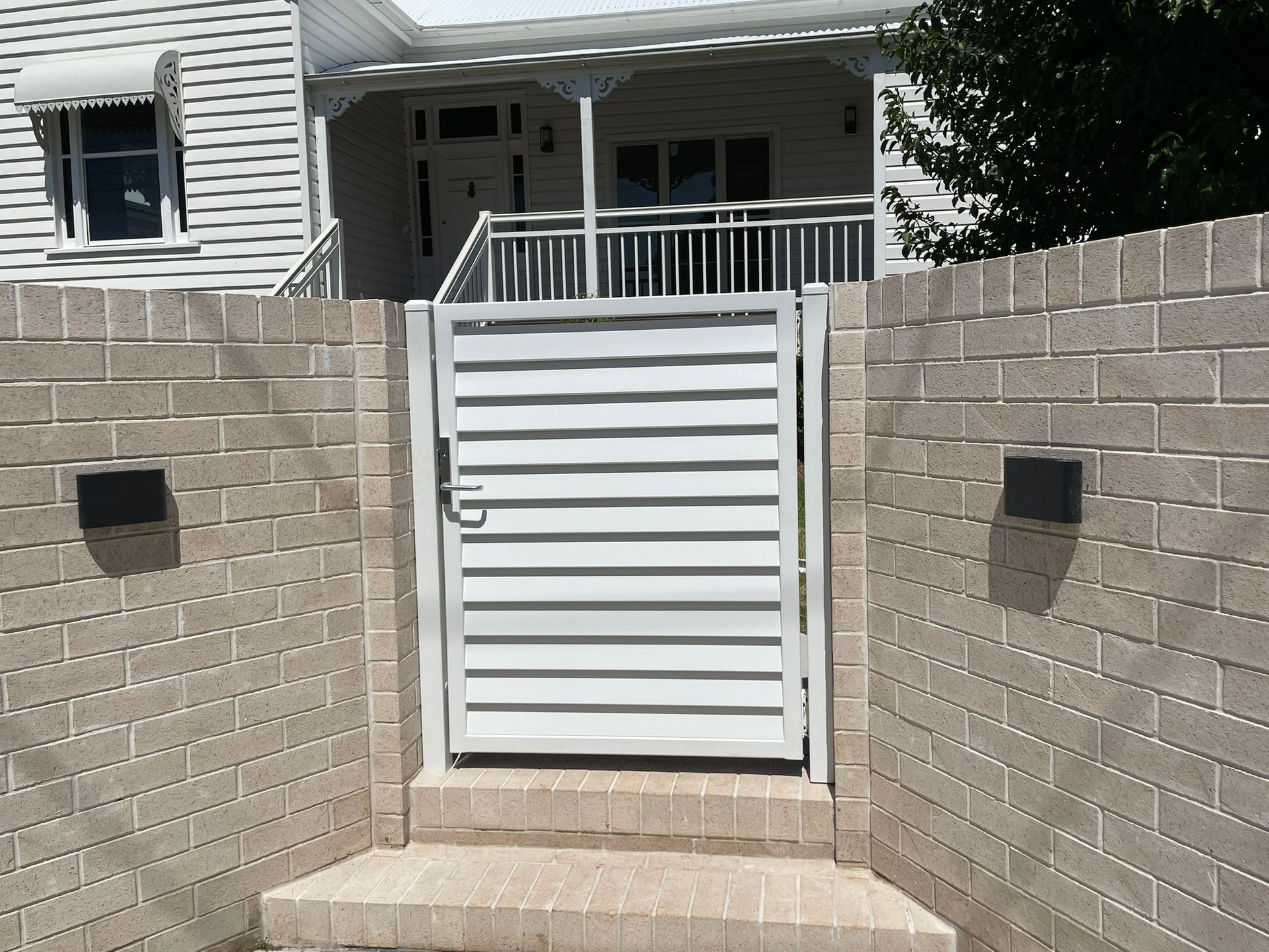 A brick wall with a white gate leading to a house