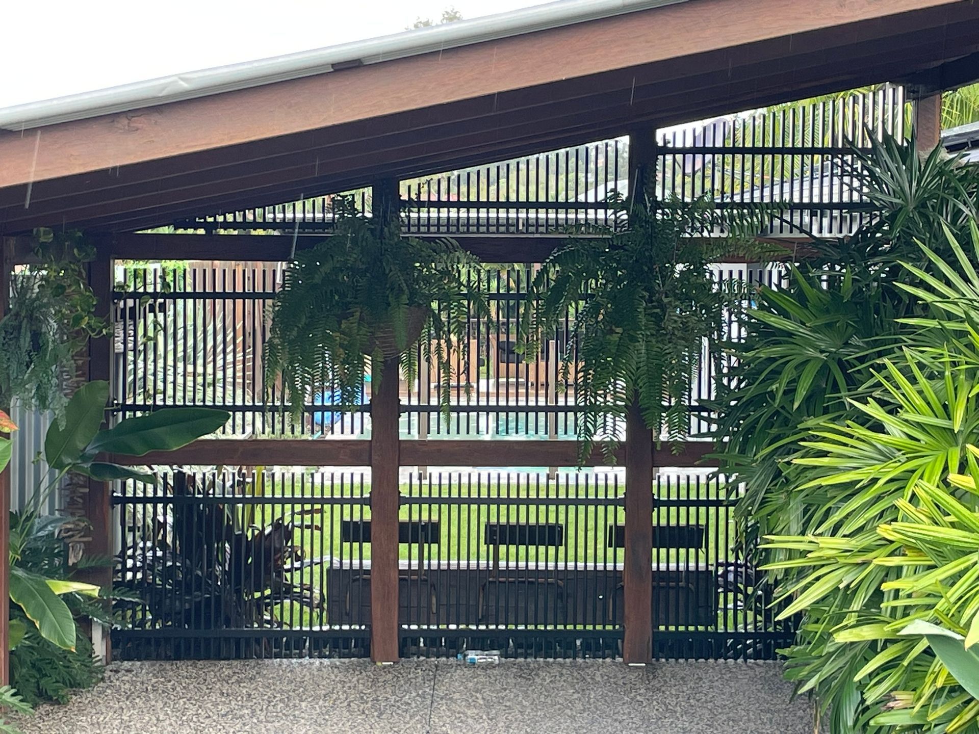 A fence with a wooden roof is surrounded by plants and trees.