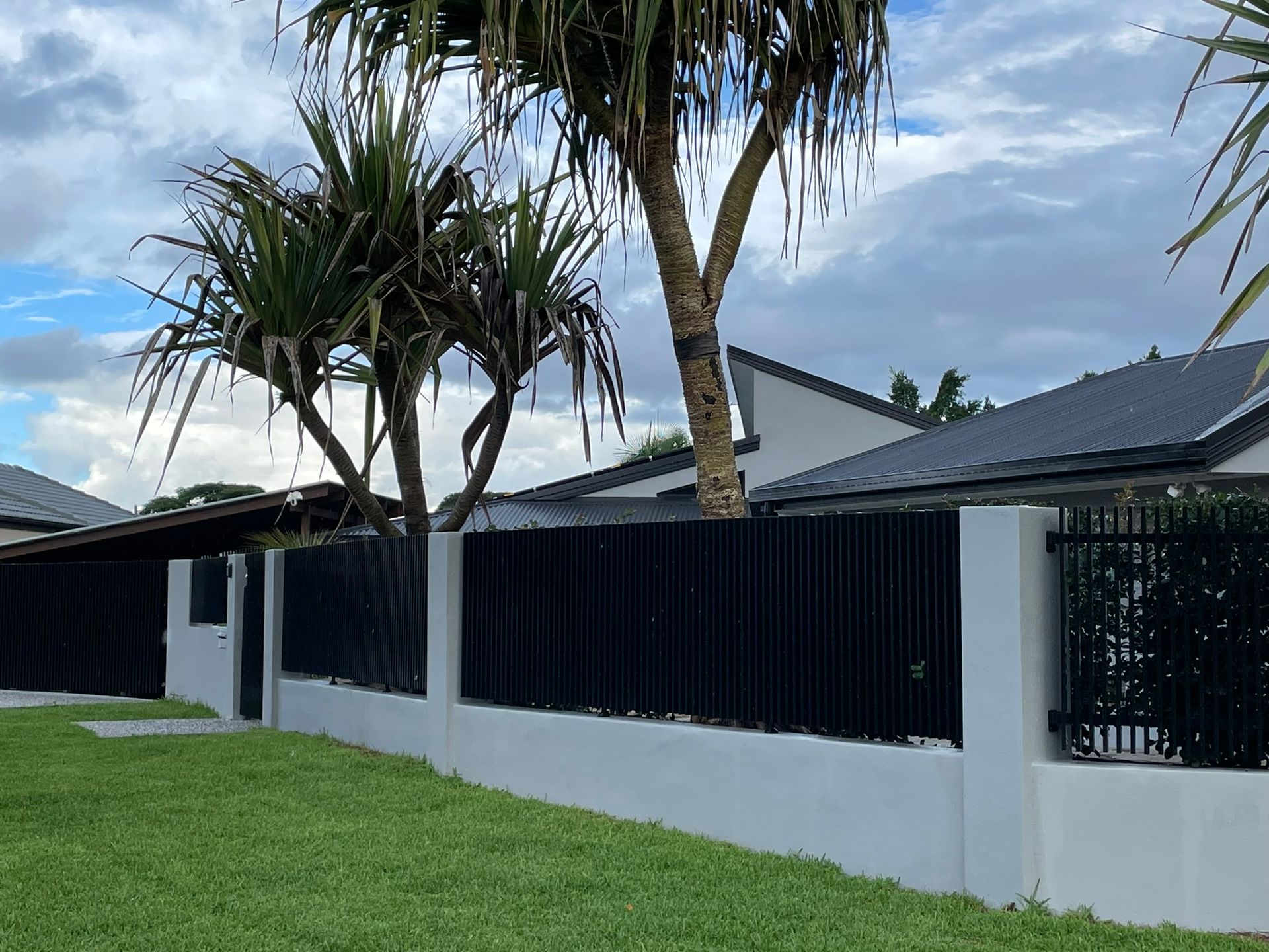 A black fence surrounds a lush green lawn in front of a house.