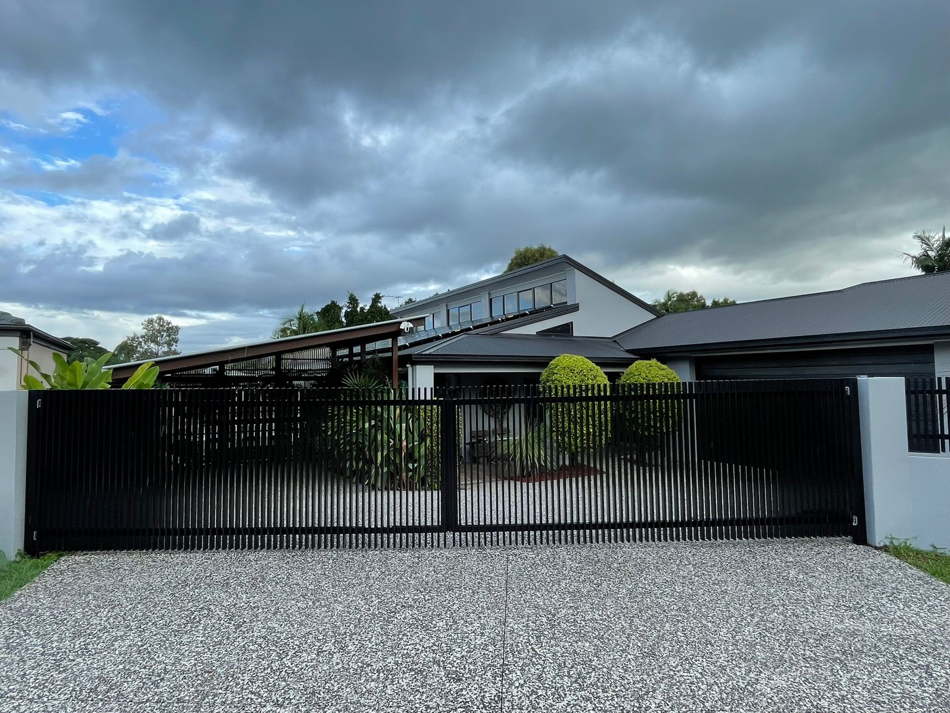 A house with a black fence and a gravel driveway in front of it.
