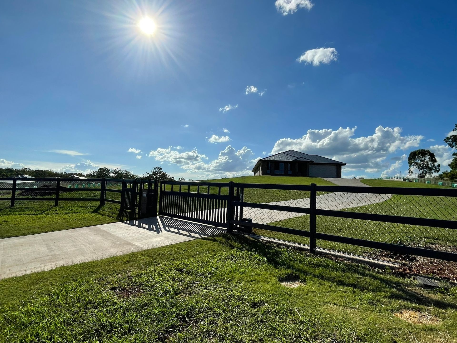 A fence surrounds a grassy field with a house in the background.