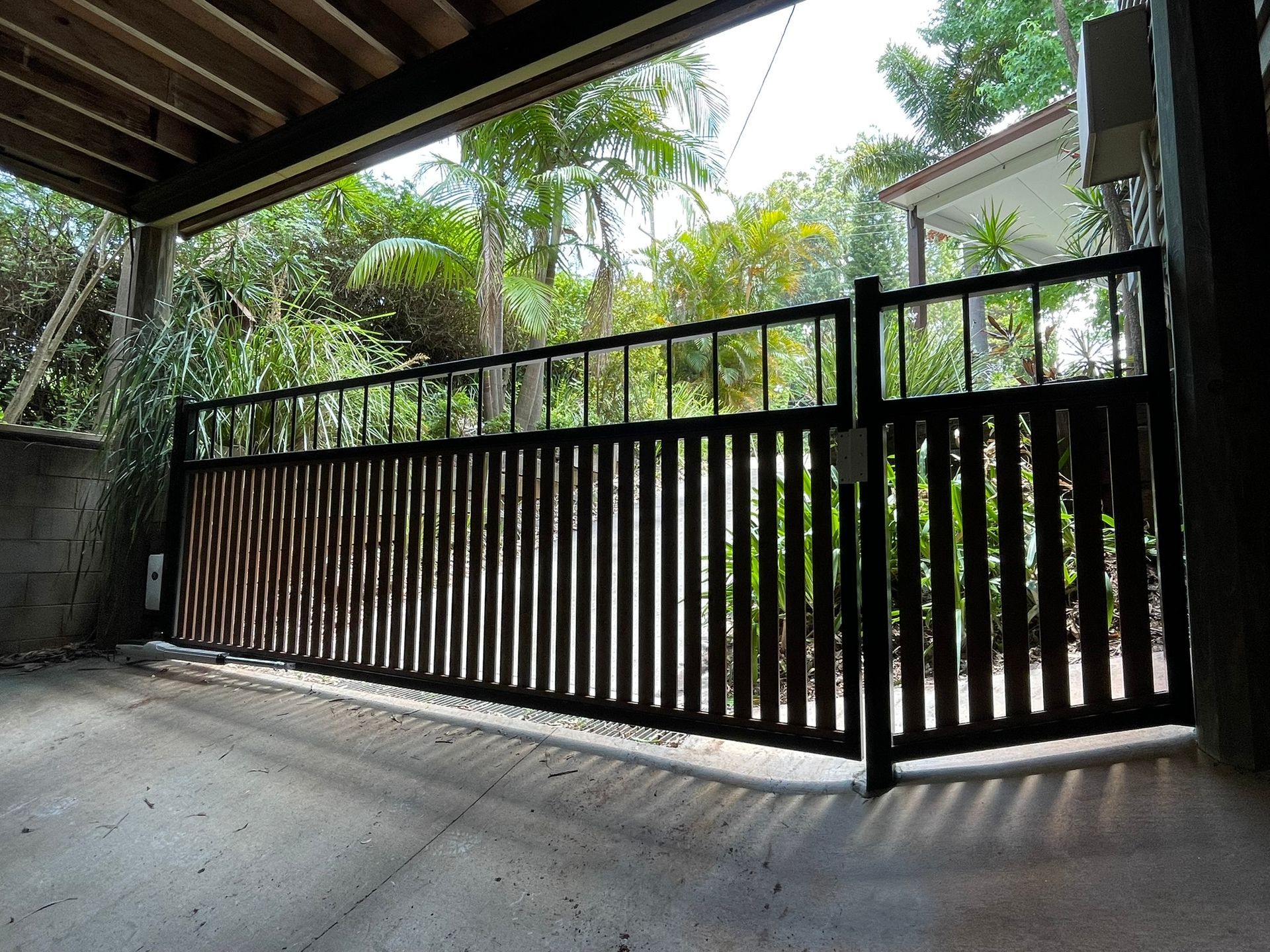 A wooden gate is open in a driveway with trees in the background