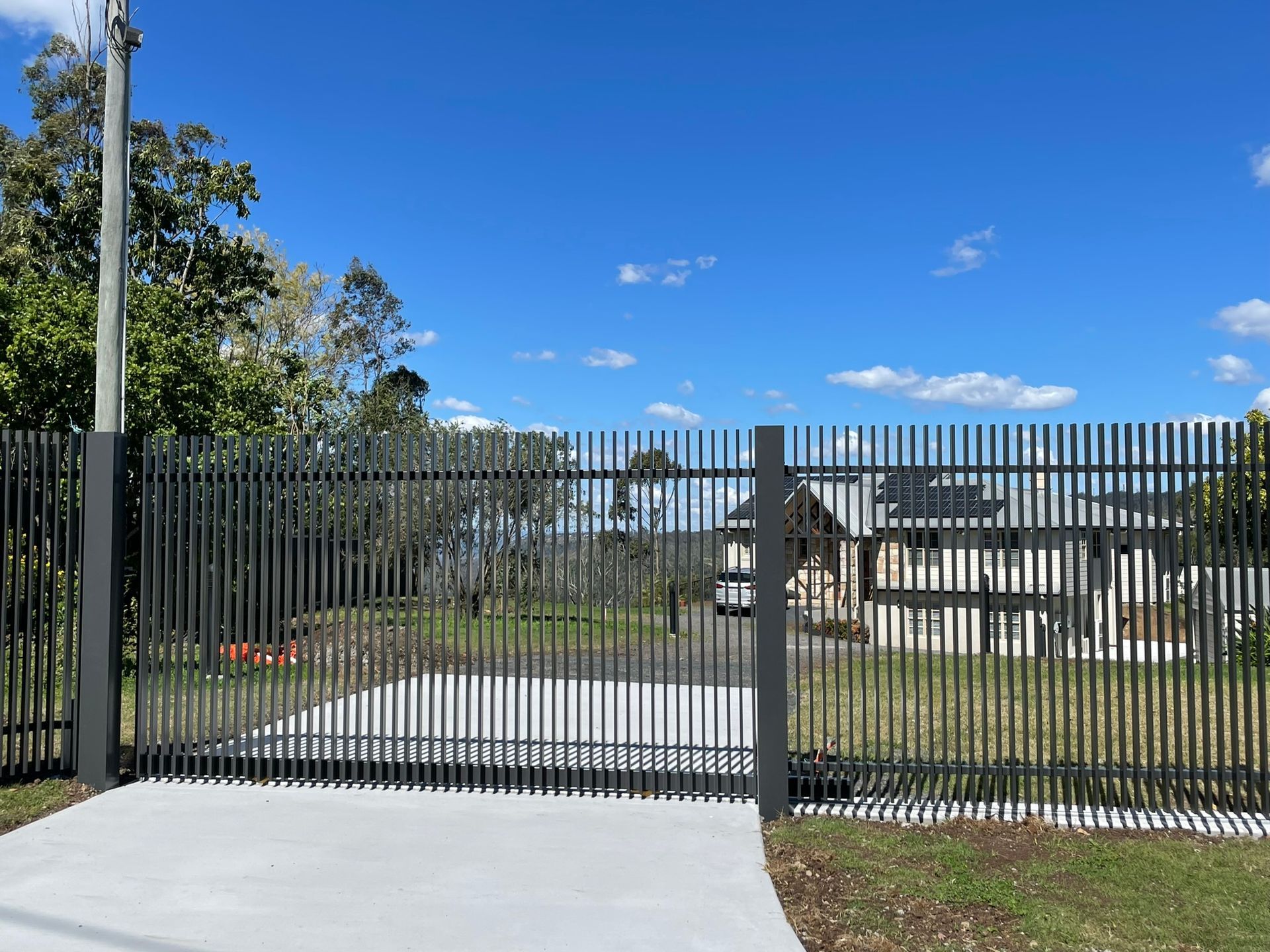 A fence with a concrete driveway leading to a house.