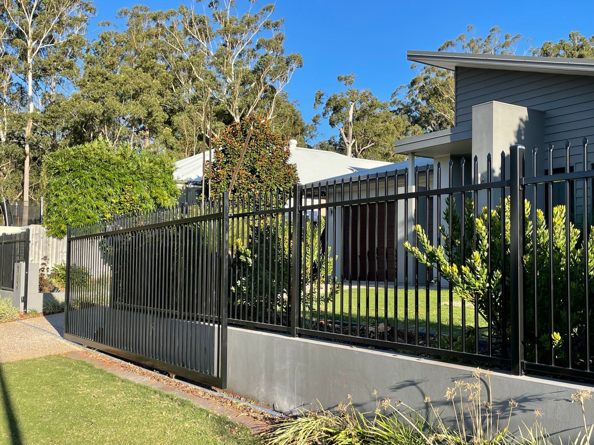 A black metal fence surrounds a house with trees in the background.