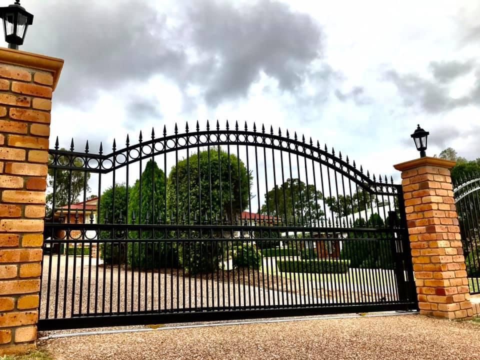 A black wrought iron gate with a brick pillar in front of it.