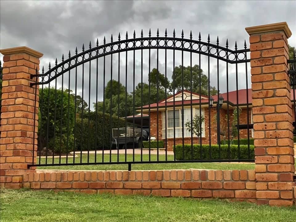 A wrought iron fence surrounds a brick wall in front of a house