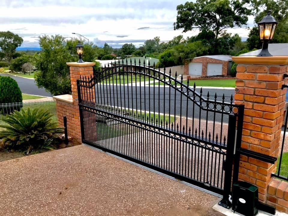 A black wrought iron gate is open to a driveway.