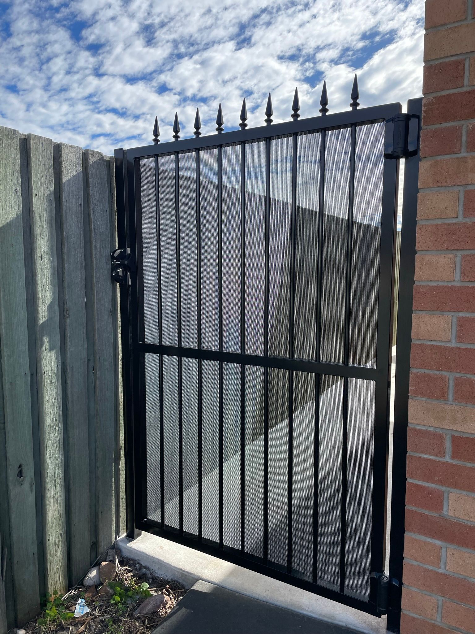 A black gate is sitting next to a brick wall.