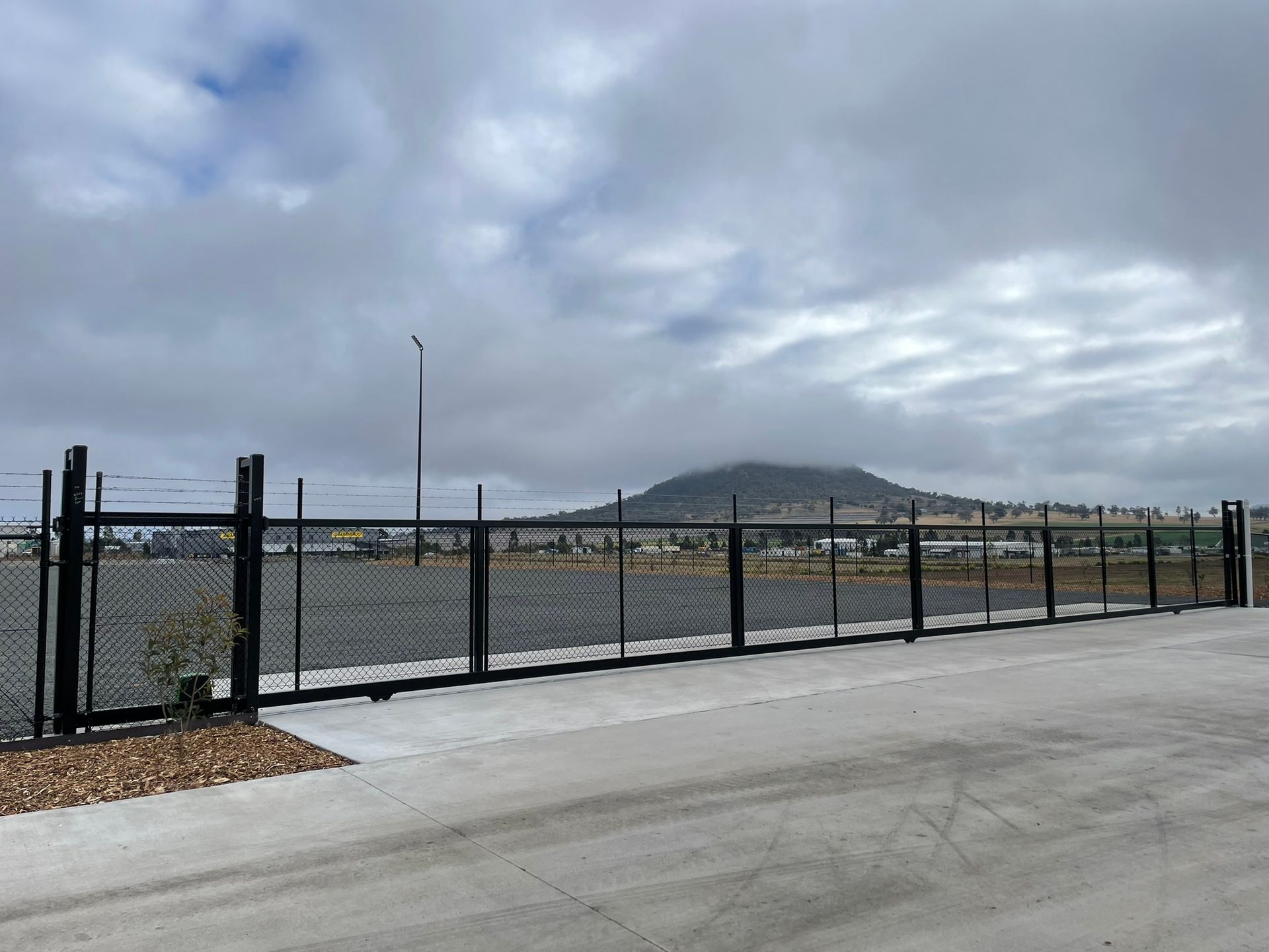 A fence is surrounding a parking lot with a mountain in the background.