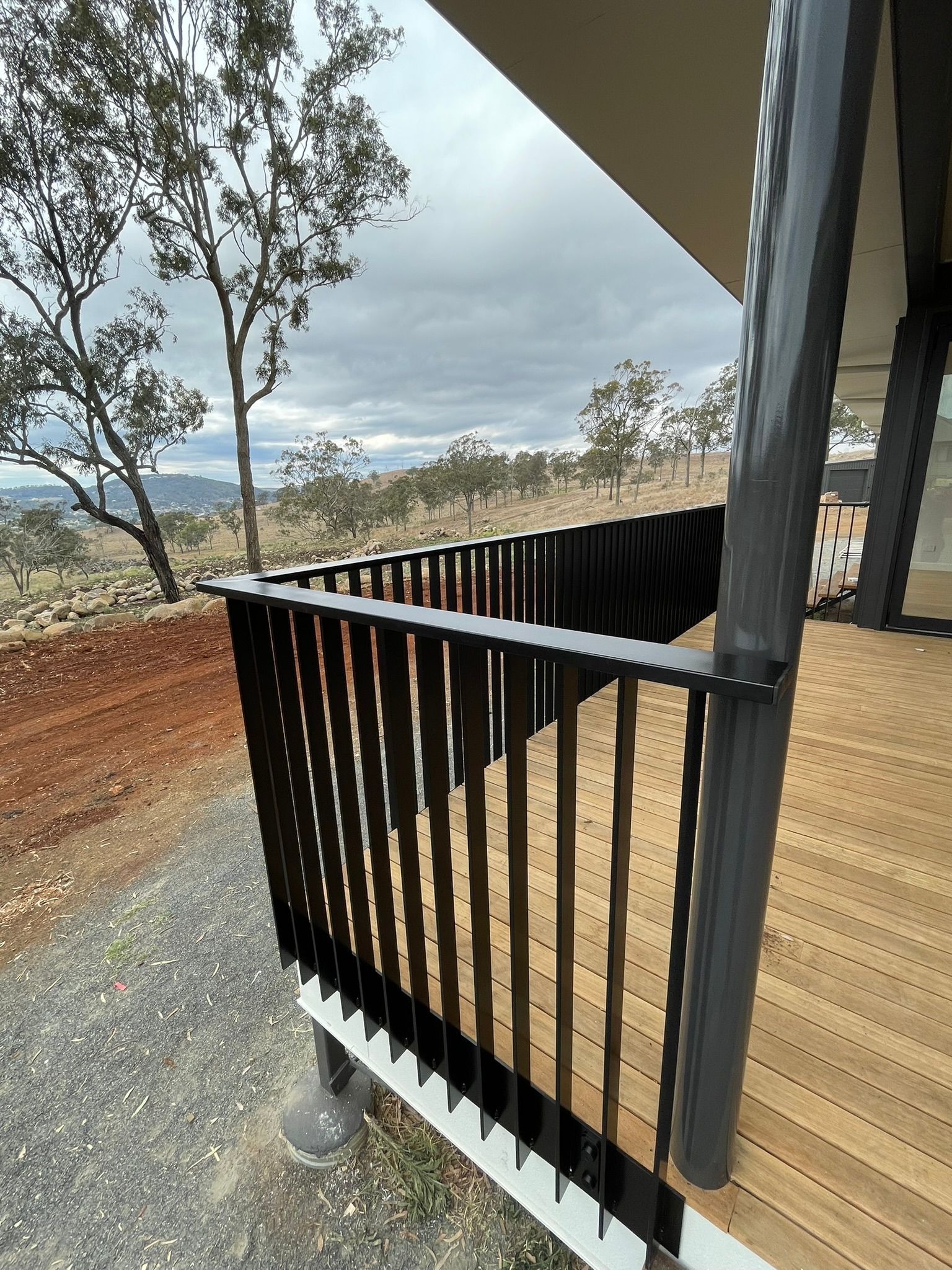A wooden deck with a black railing and trees in the background.