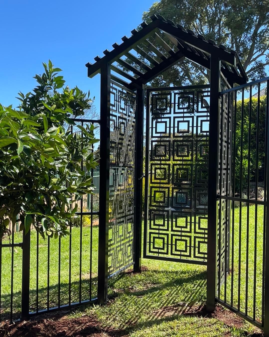 A black gate with a geometric design is surrounded by a fence