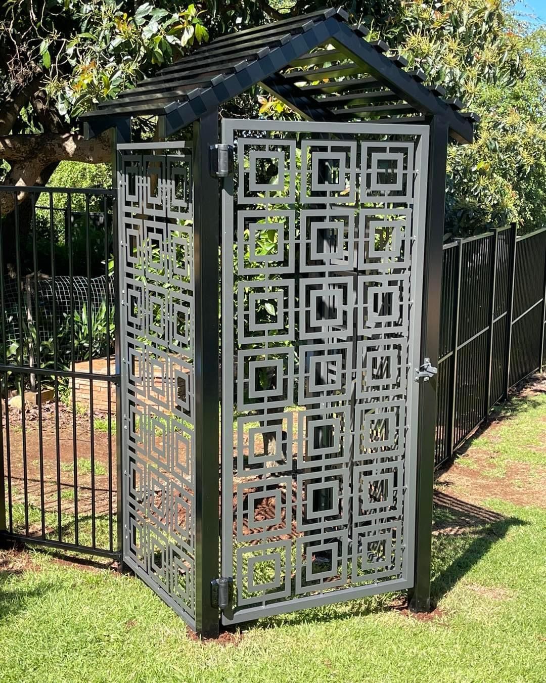 A metal gate with a pattern on it is sitting on top of a lush green lawn next to a fence.