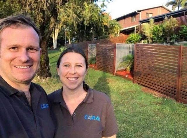Dale and Helen are posing for a picture in front of a custom fence that they built.