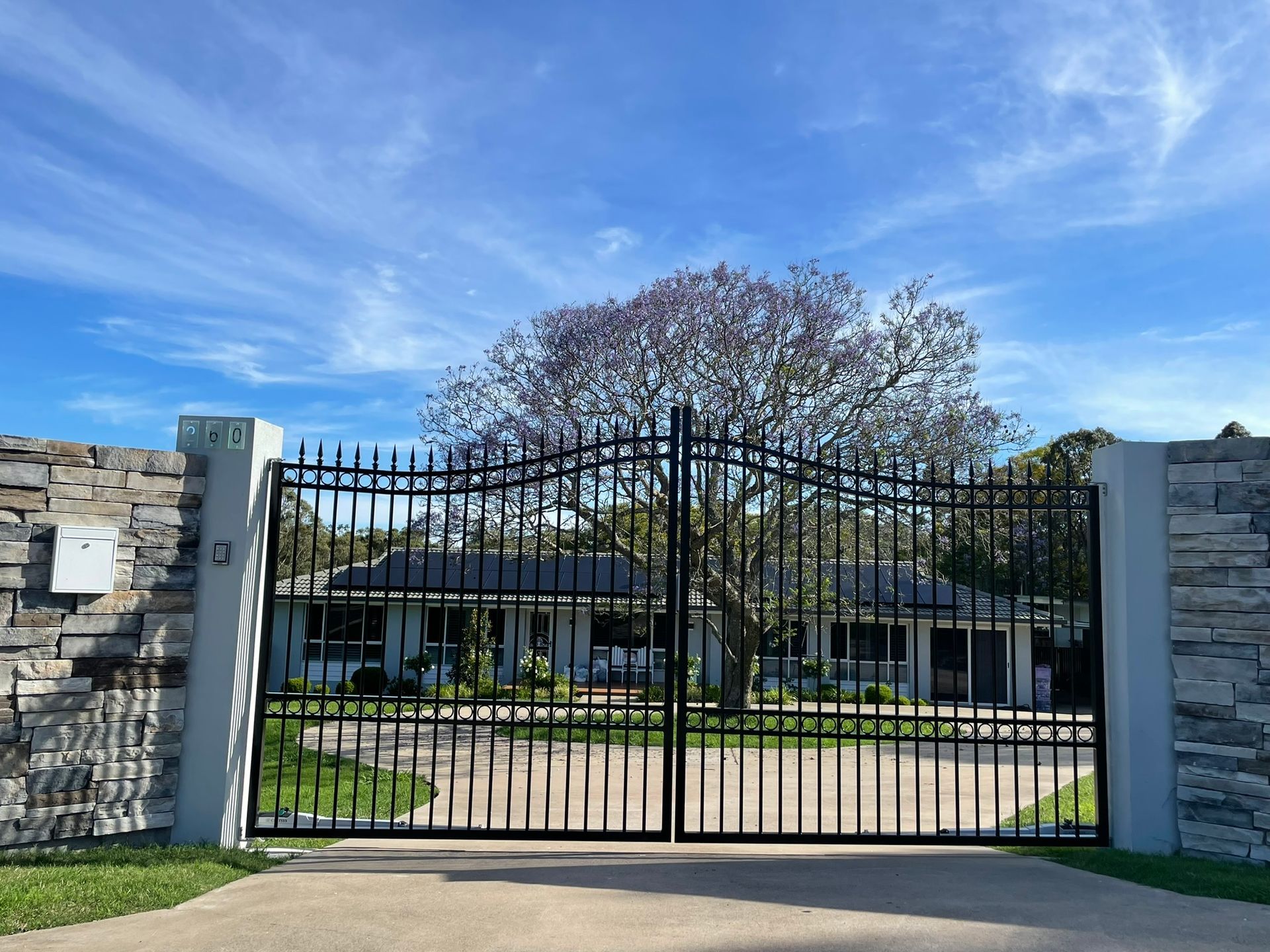 A black wrought iron gate is leading to a house.
