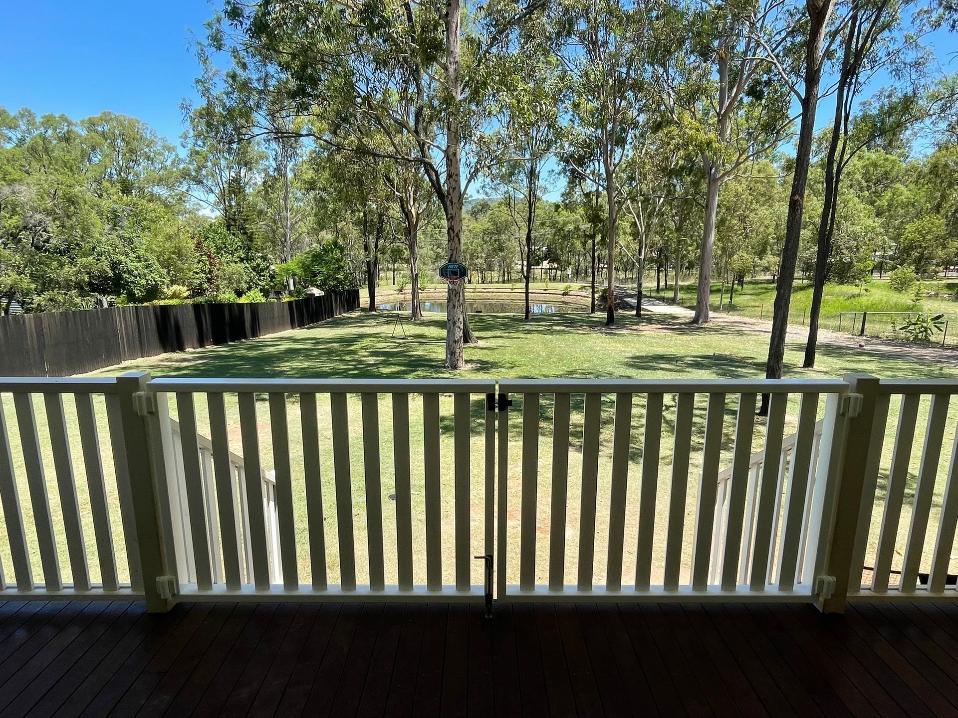 A view of a park from a deck with a fence and trees in the background.