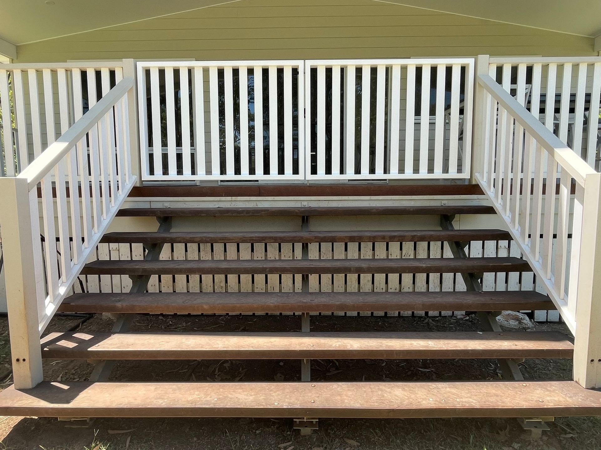 A set of stairs leading up to a veranda with a white railing