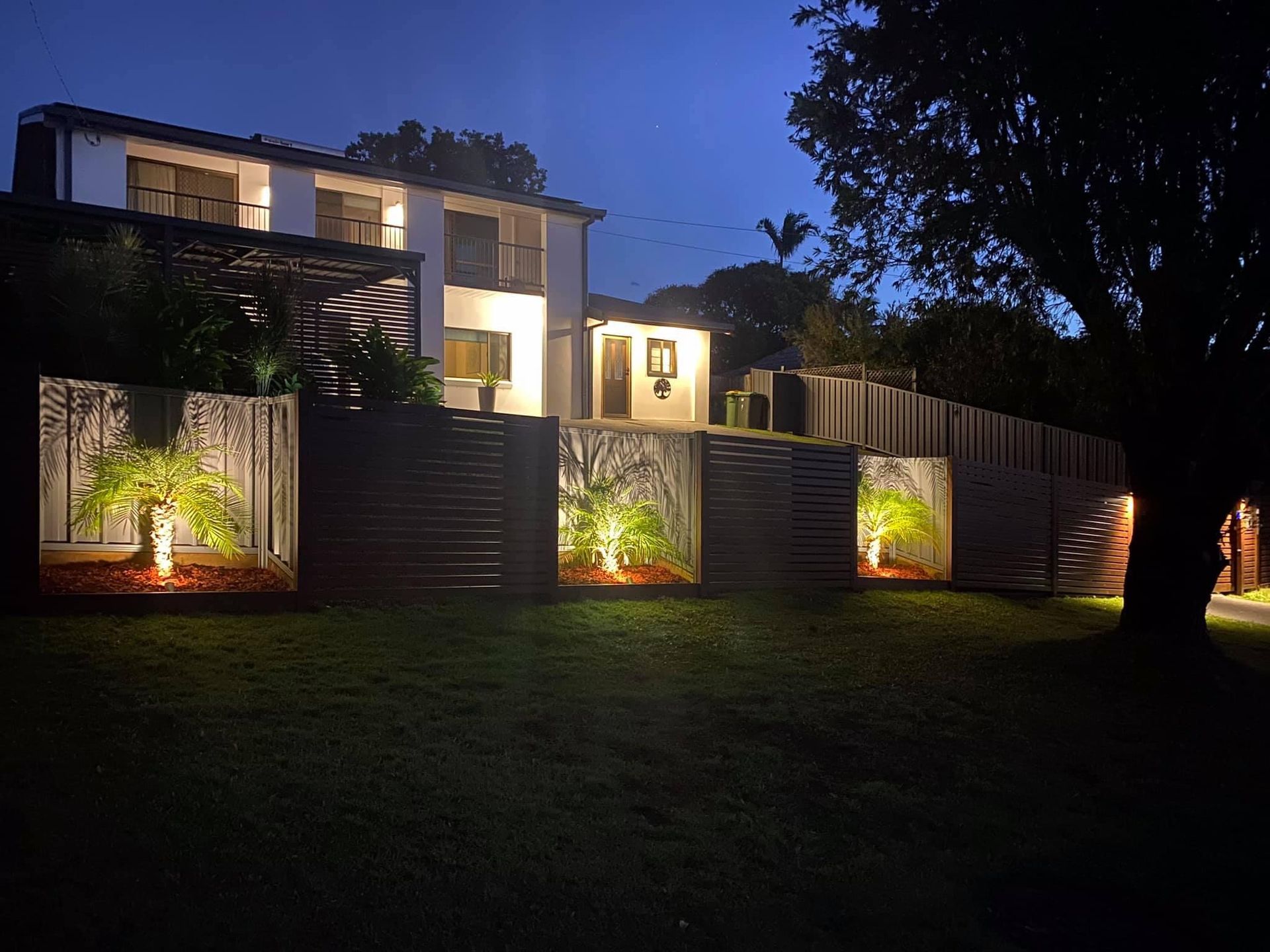 A house is lit up at night with trees in front of the new custom fence.