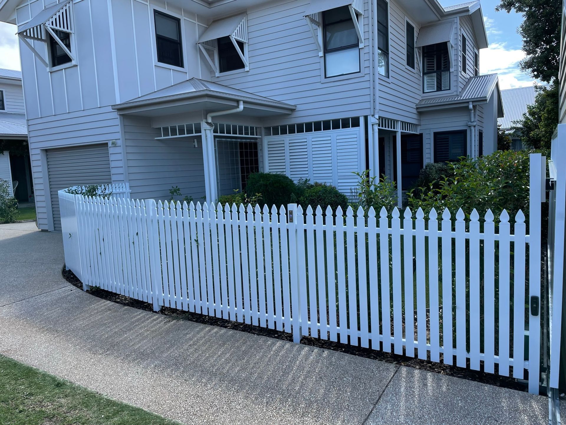 A white picket fence is in front of a white house.