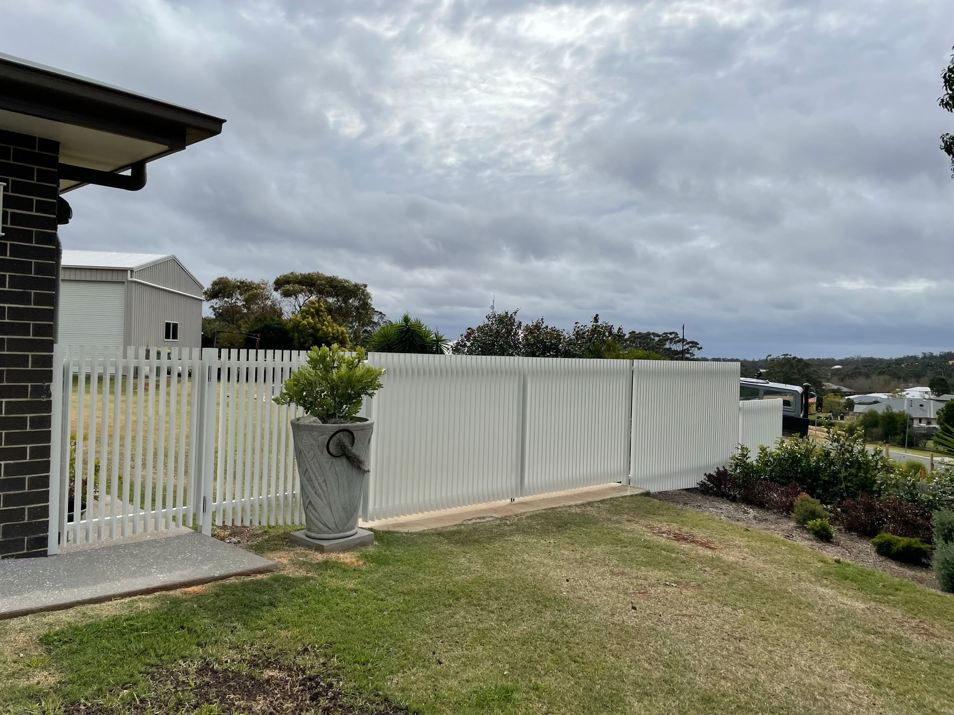 A white picket fence surrounds a lush green yard in front of a house.