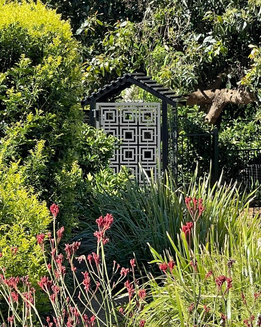 There is a gate in the middle of a garden surrounded by trees and flowers.