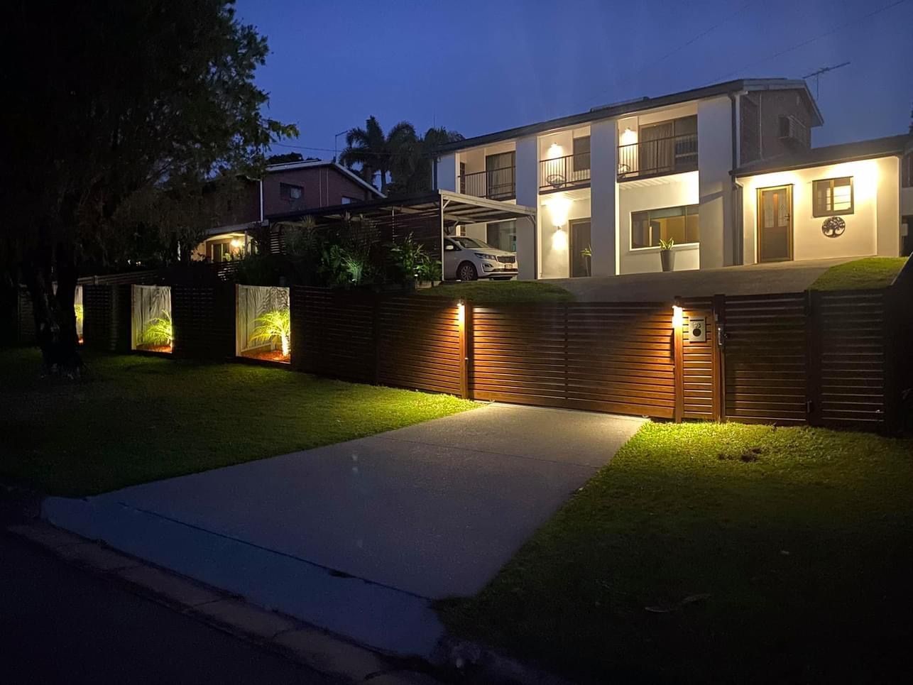 A house with a new fence and a car parked in front of it is lit up at night.