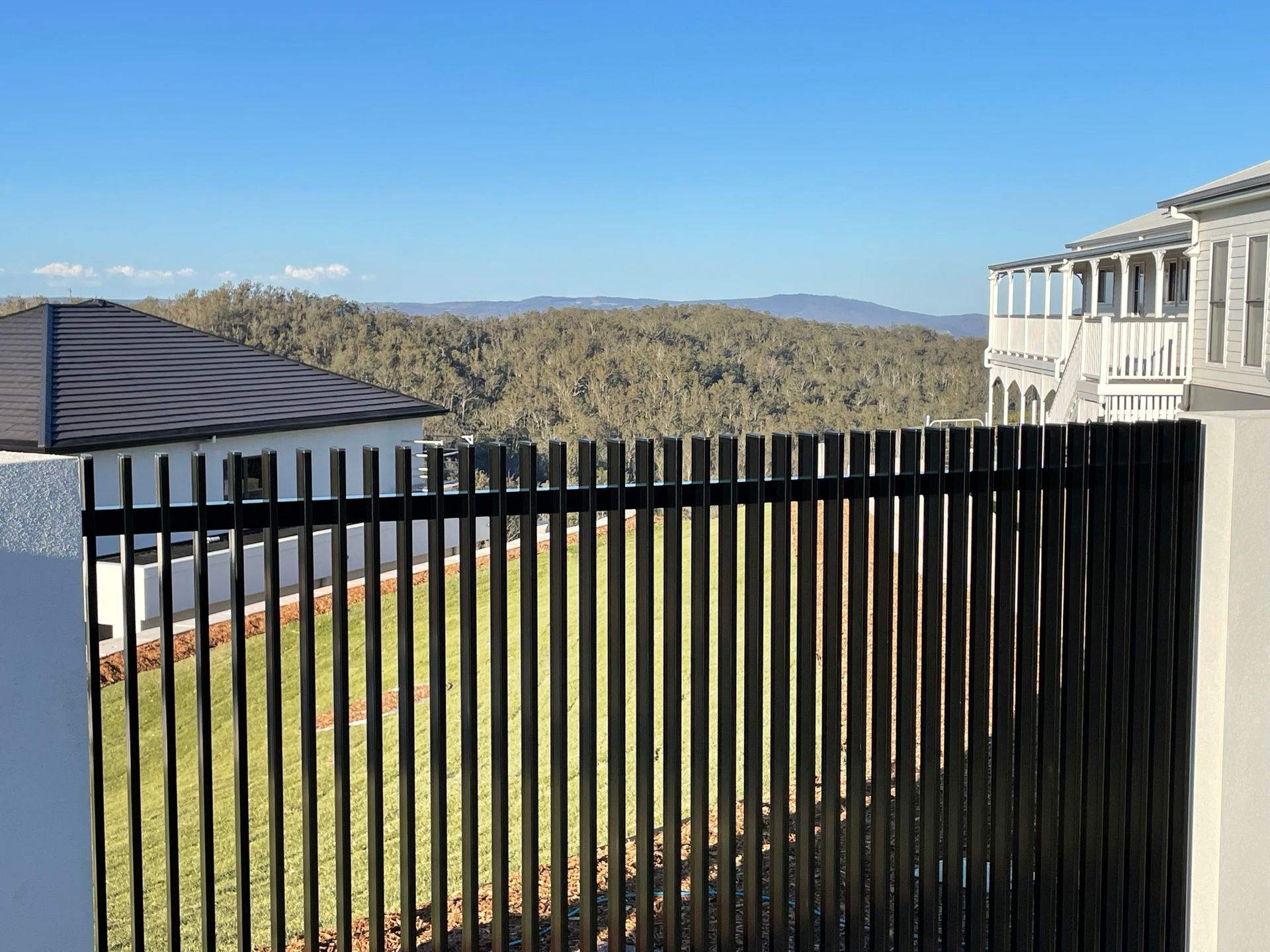 A black fence with a view of a house and mountains behind it.