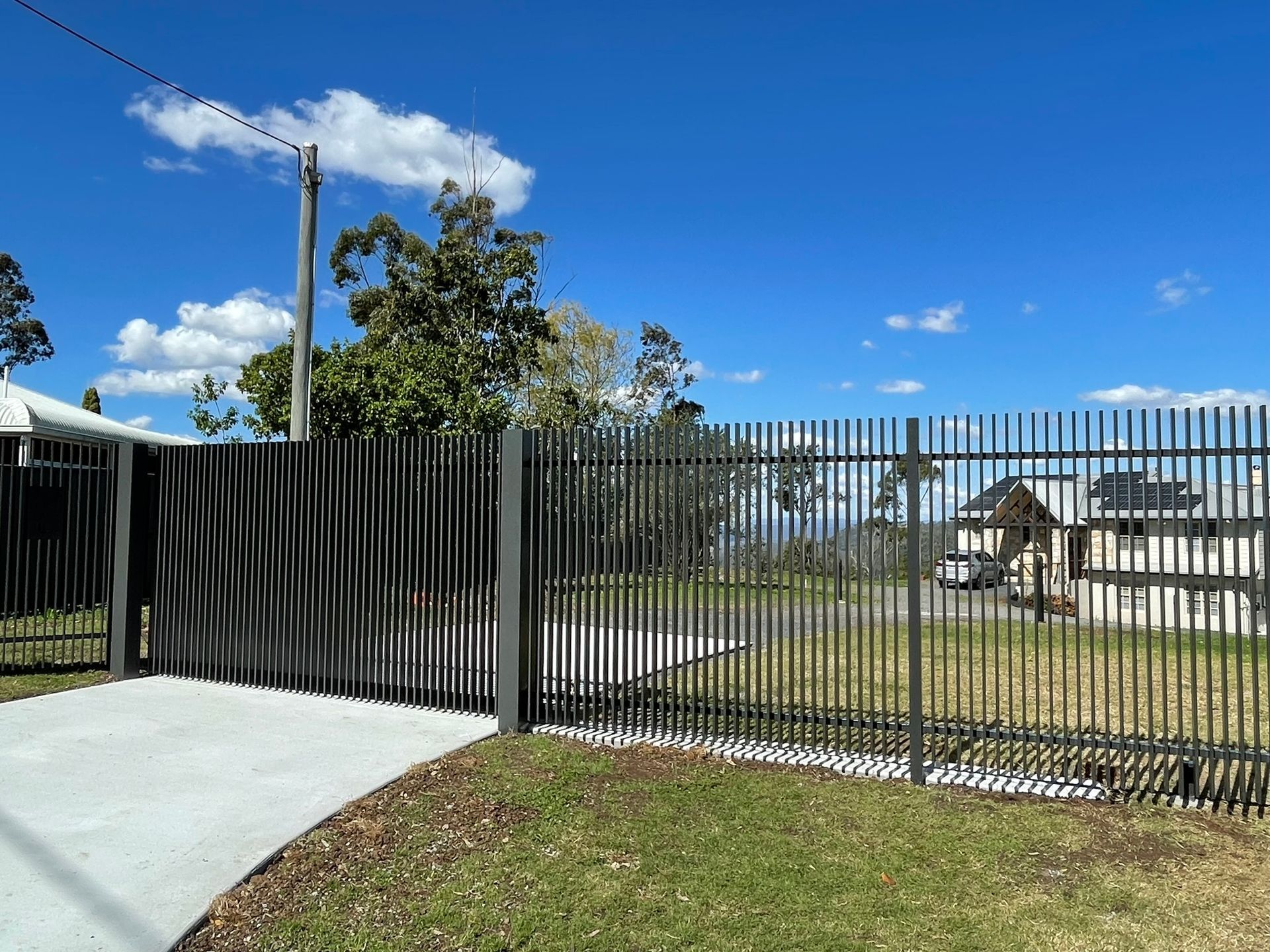 A black metal fence surrounds a driveway in front of a house.