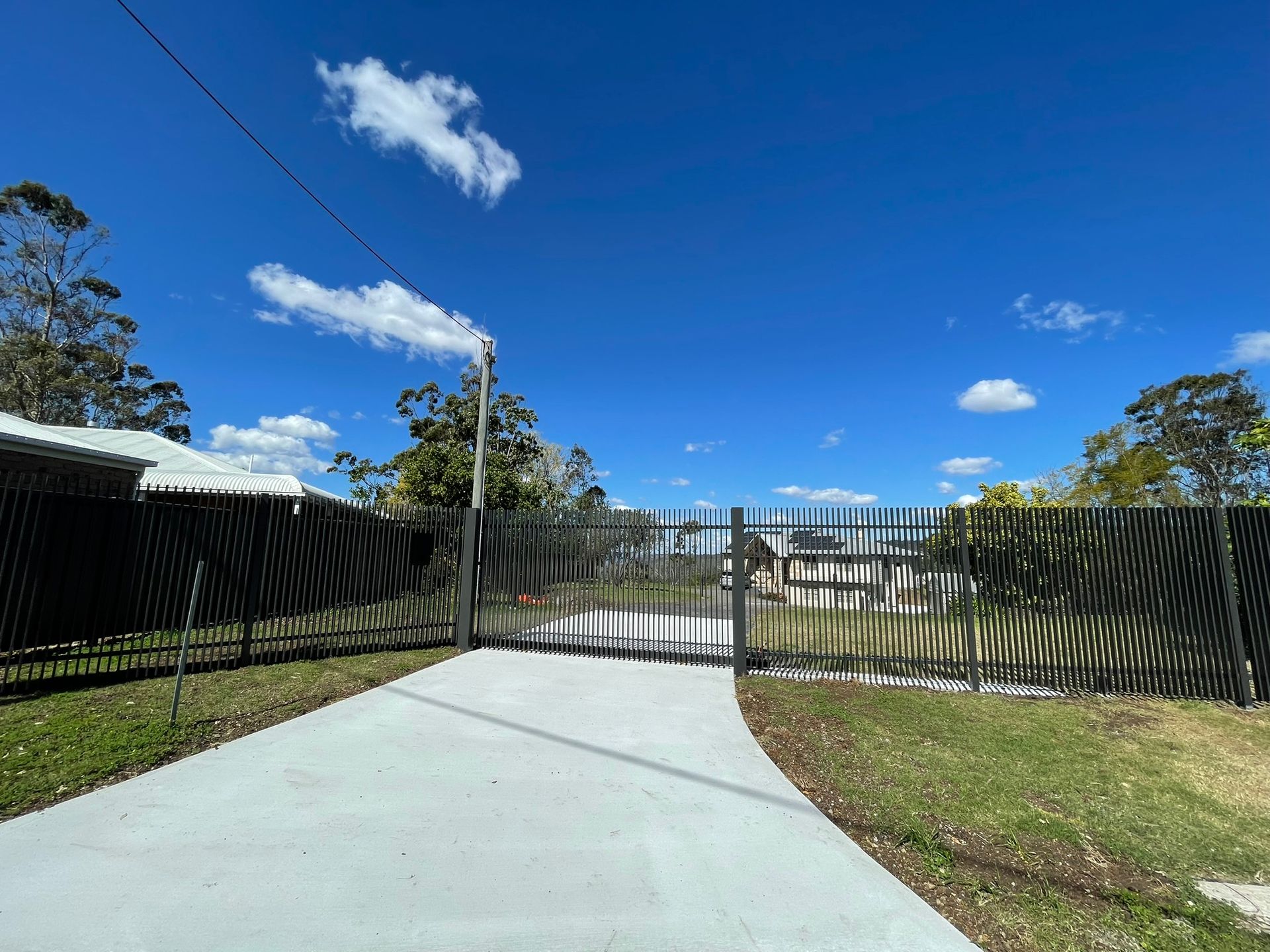 A concrete driveway leading to a fence with a blue sky in the background.