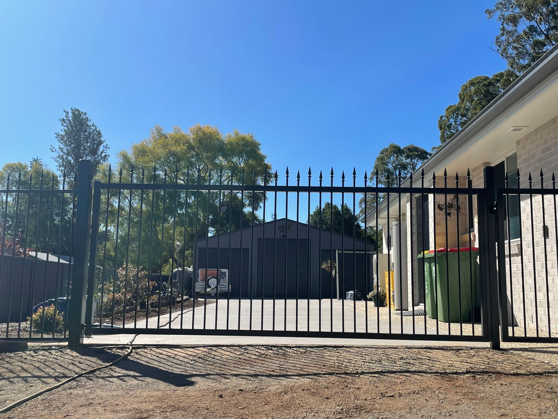 A black gate is open to a driveway in front of a house.