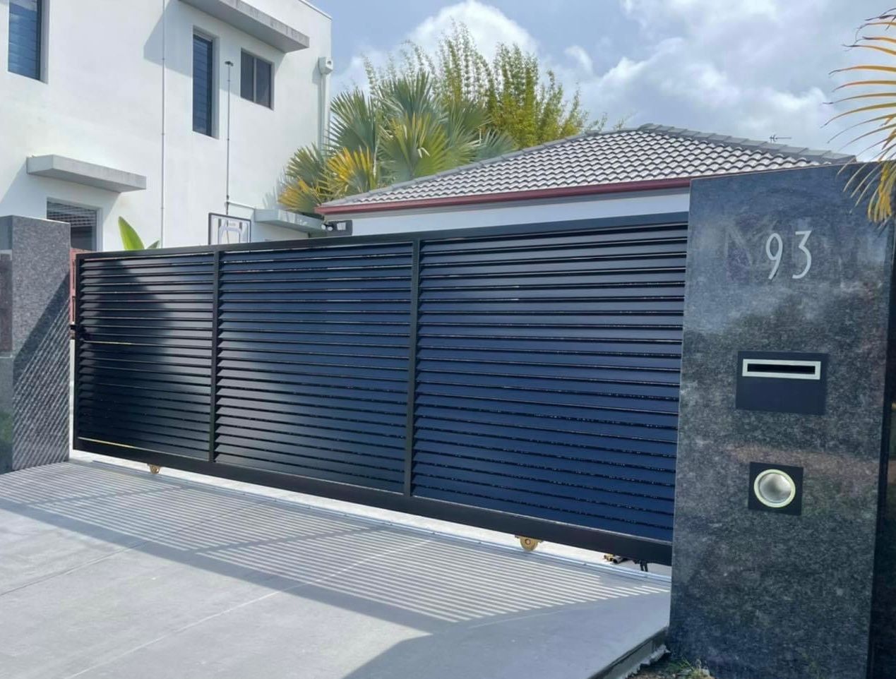 A black sliding gate is leading to a house.