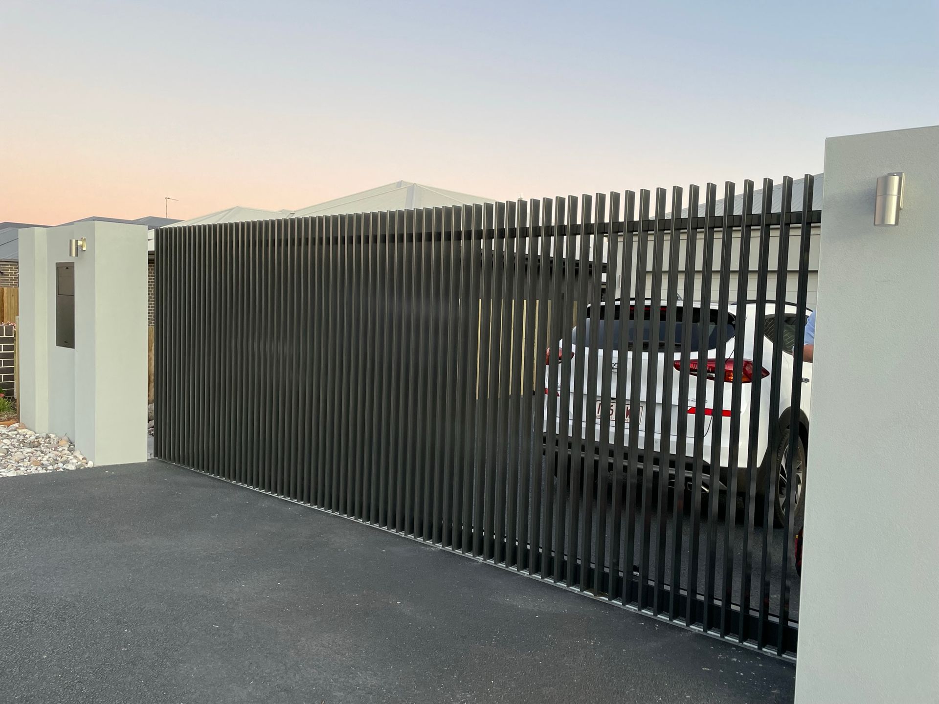A white car is parked behind a black fence.