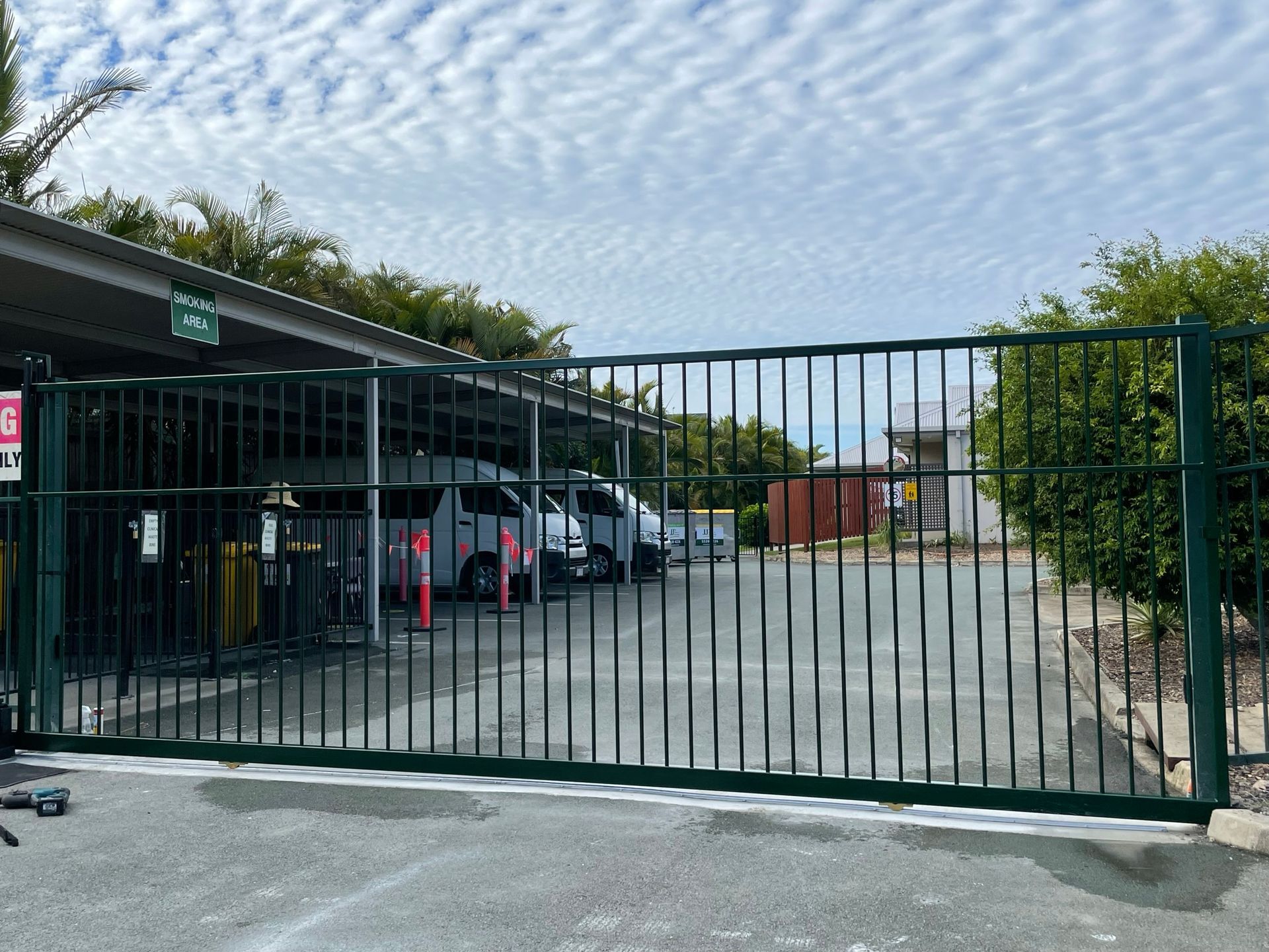 A green fence surrounds a parking lot with cars parked behind it.