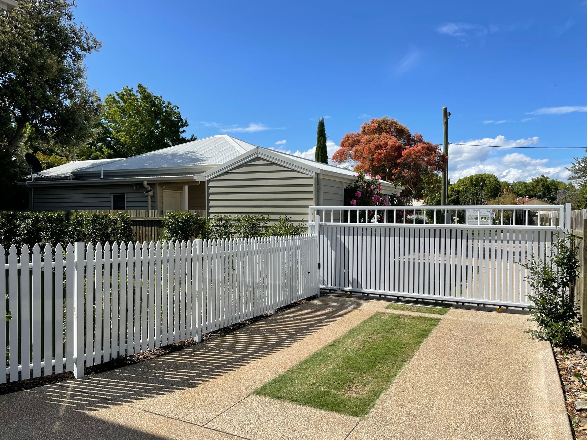 A white picket fence surrounds a driveway leading to a house.