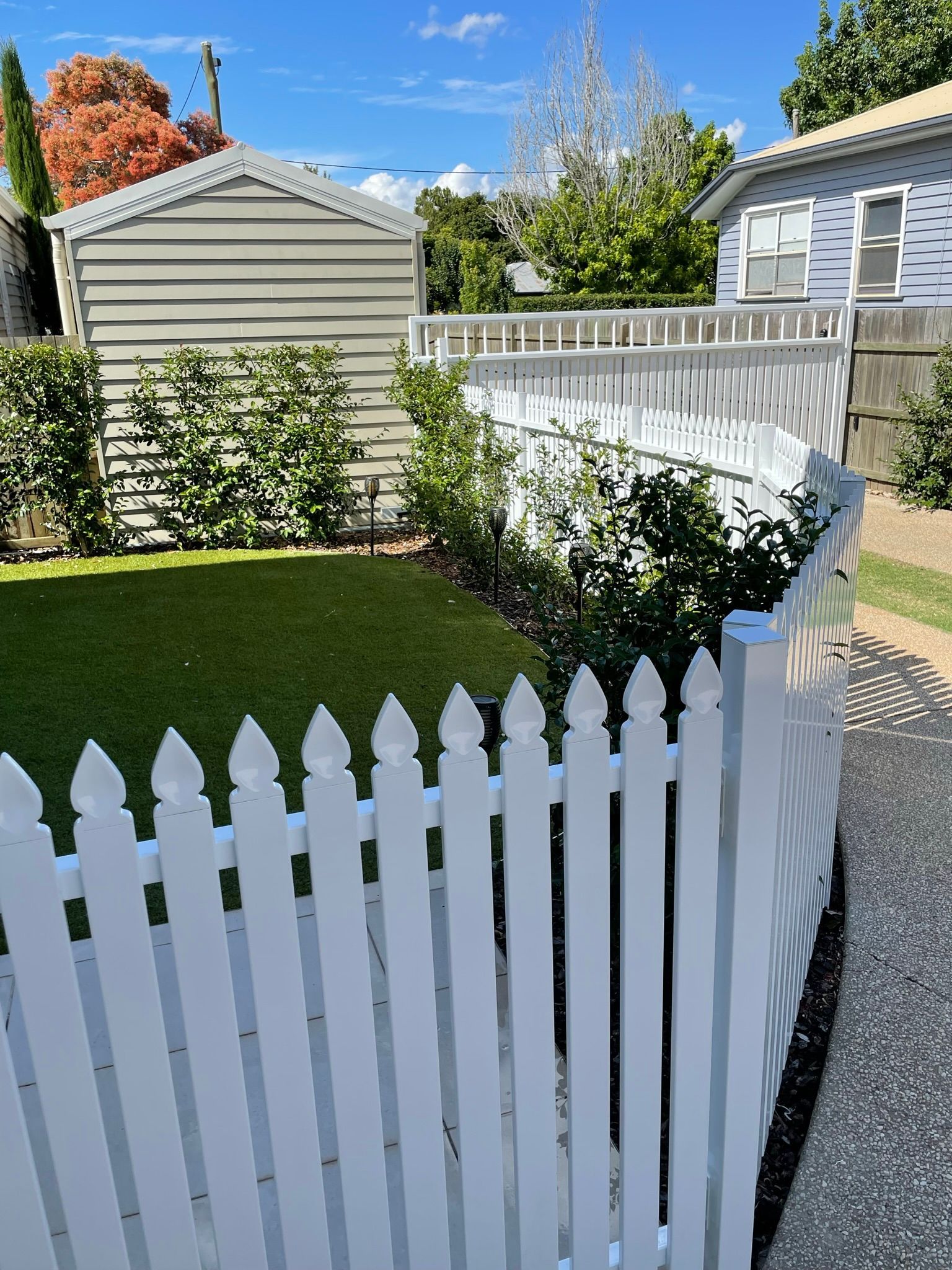 A white picket fence surrounds a lush green yard in front of a house.