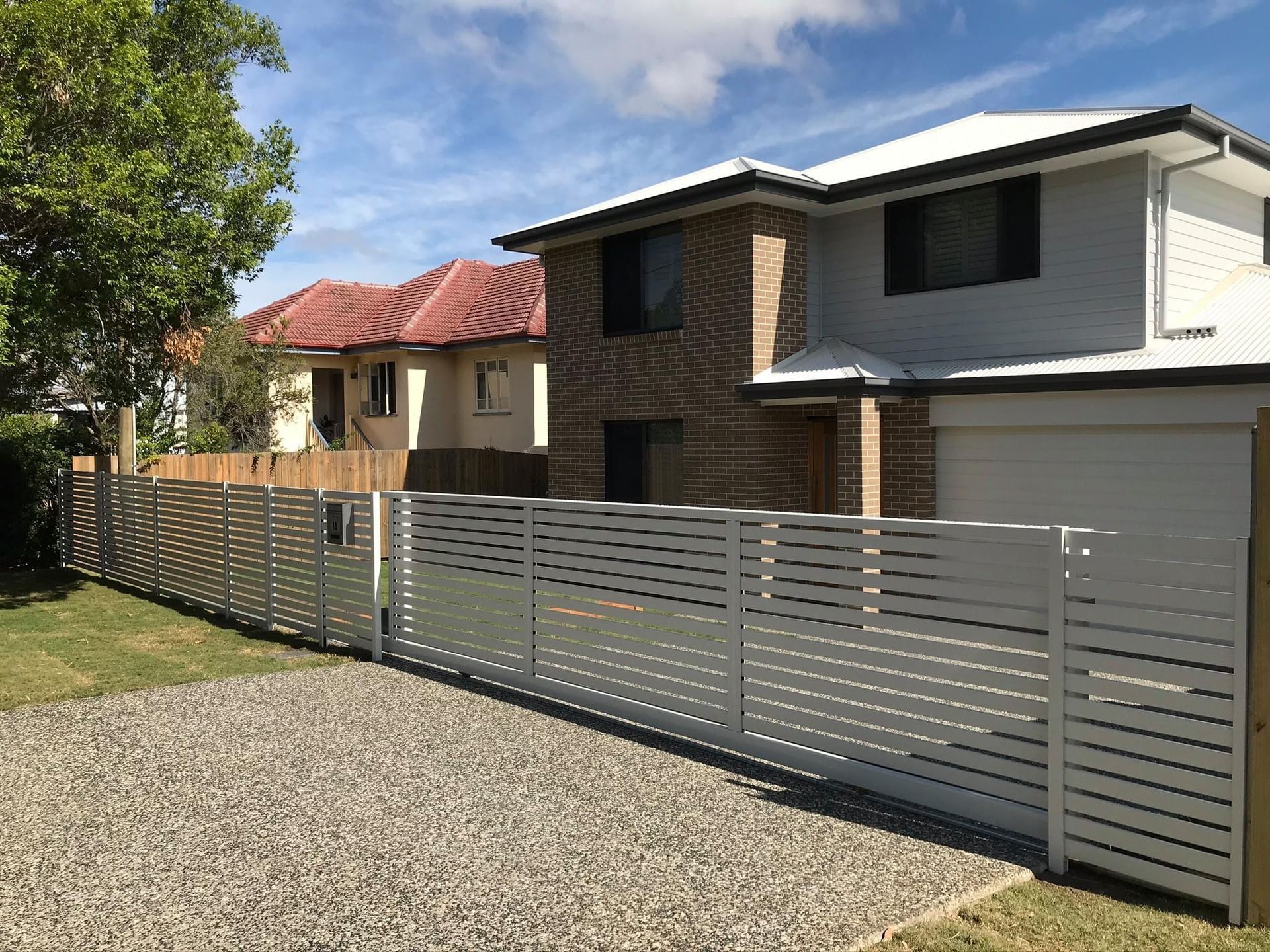A white fence surrounds a driveway in front of a house.