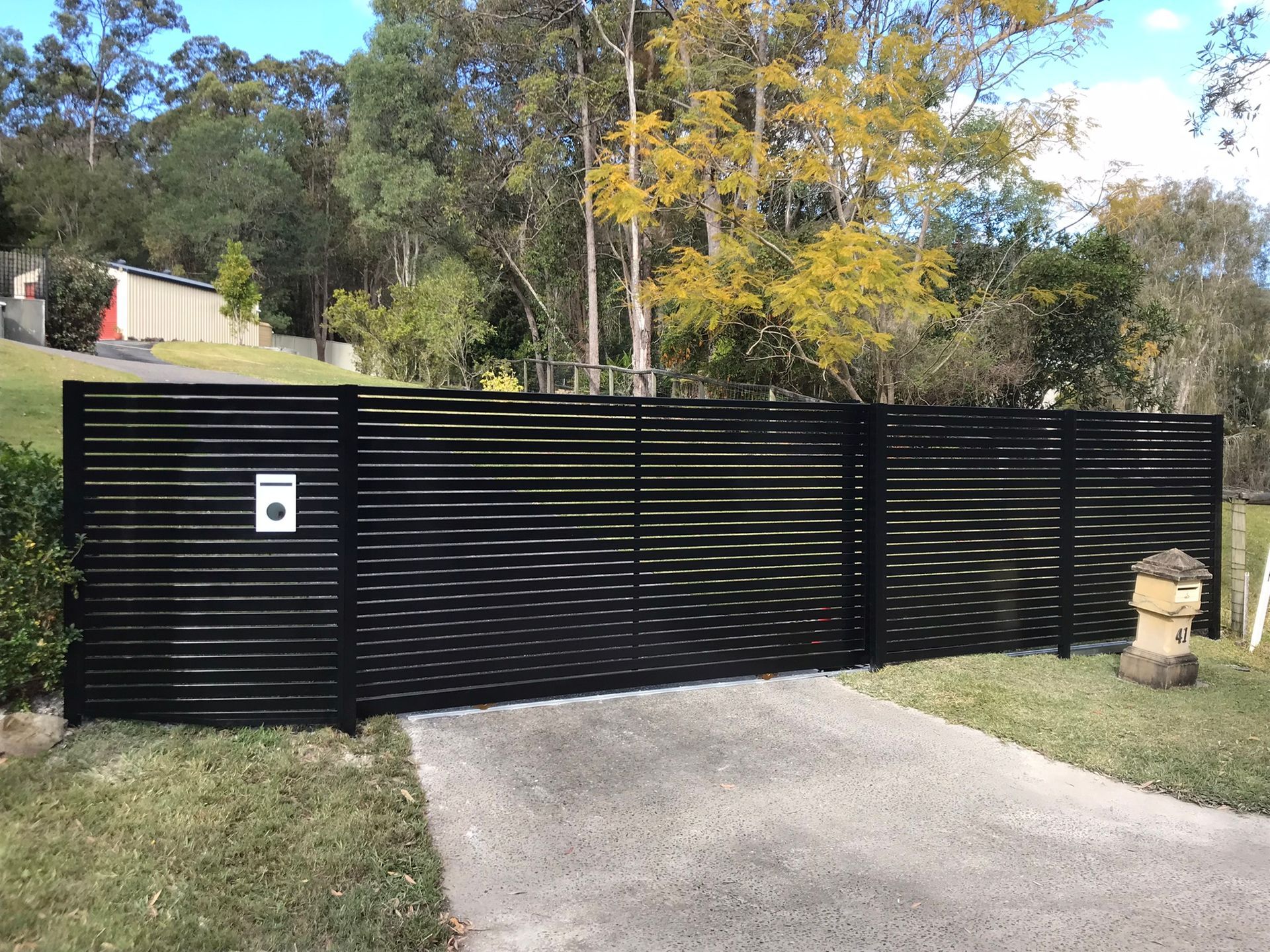 A black fence surrounds a driveway leading to a house.
