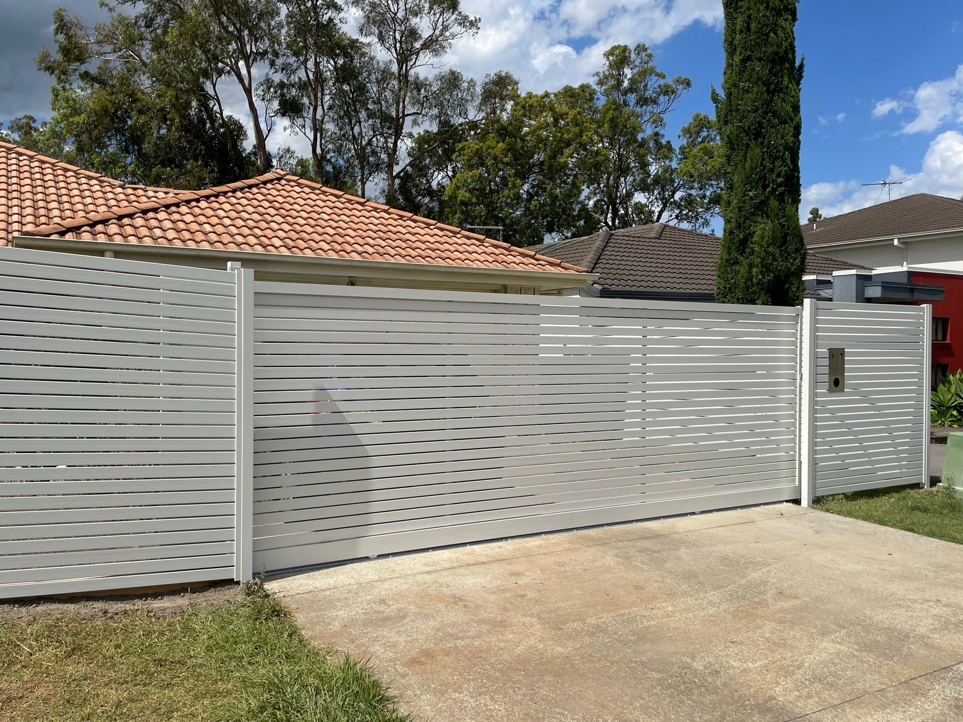 A white fence is surrounding a driveway in front of a house.