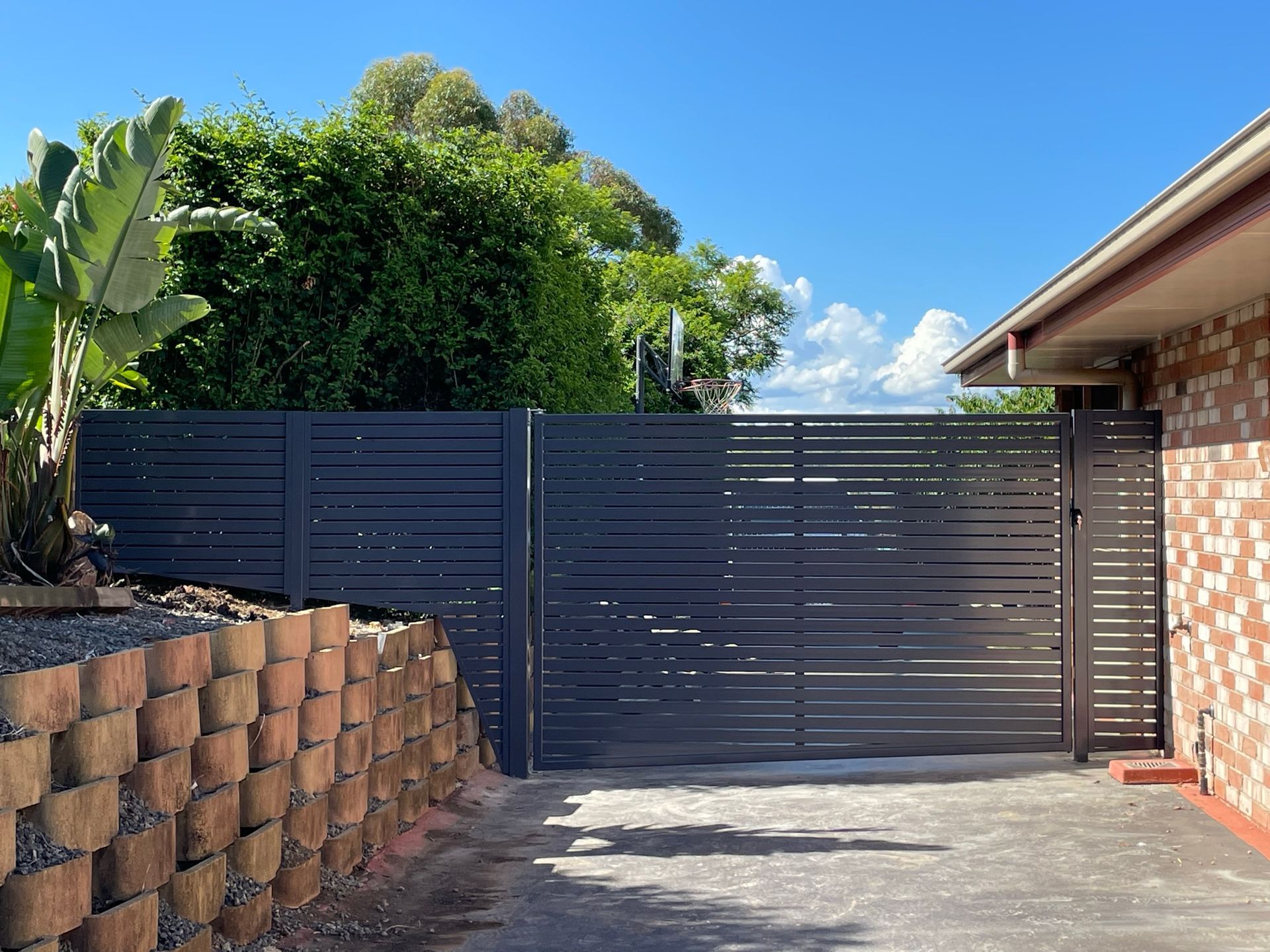 A black fence is surrounding a driveway in front of a house.