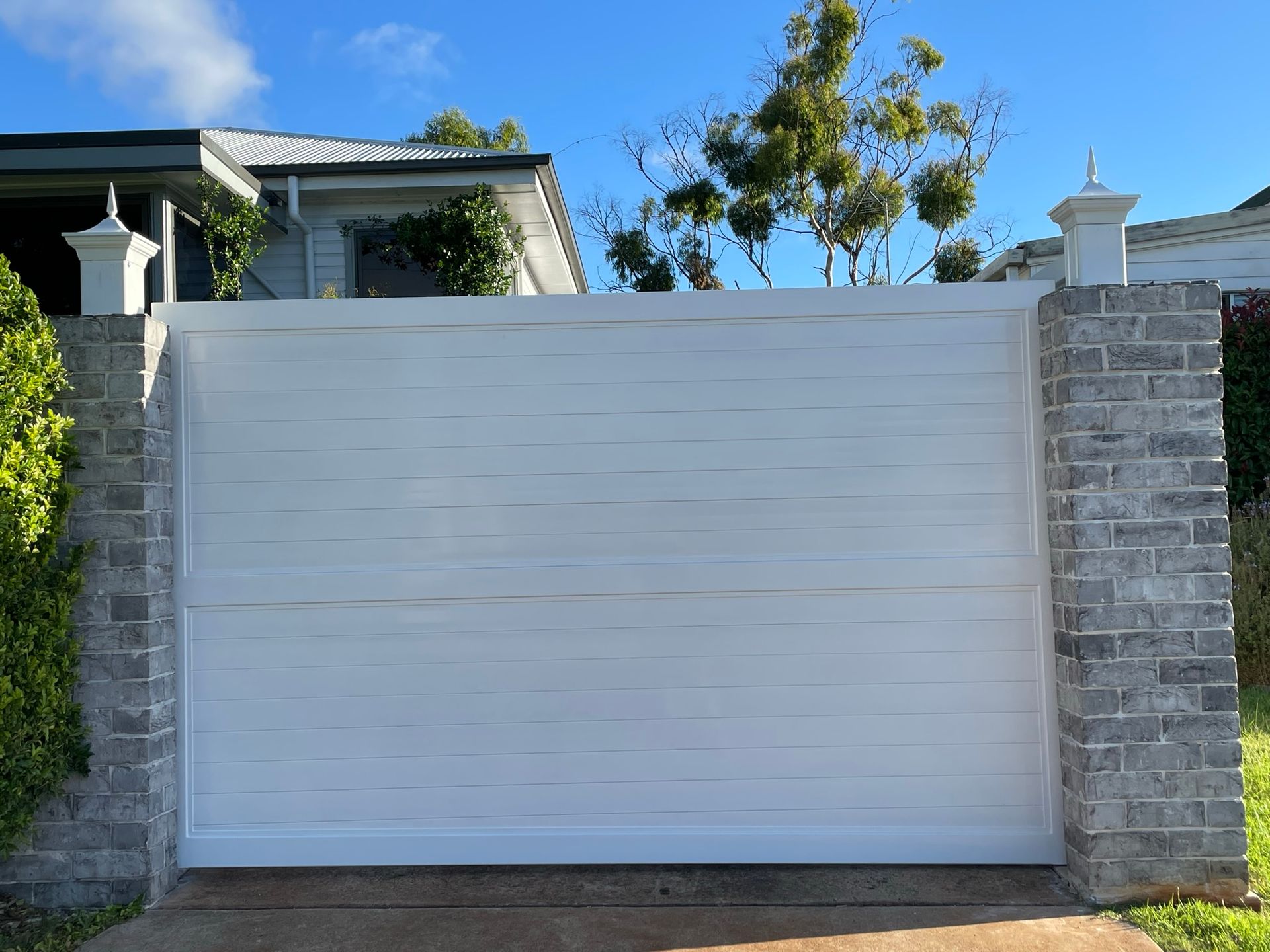 A white sliding gate is sitting next to a brick wall.