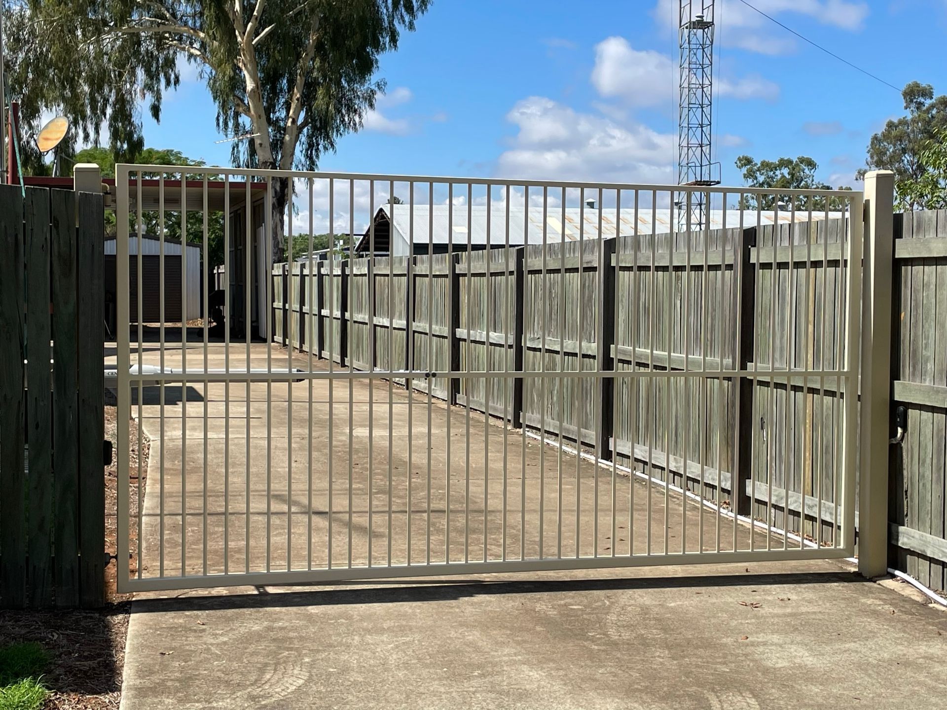 A metal gate is open to a driveway with a wooden fence behind it