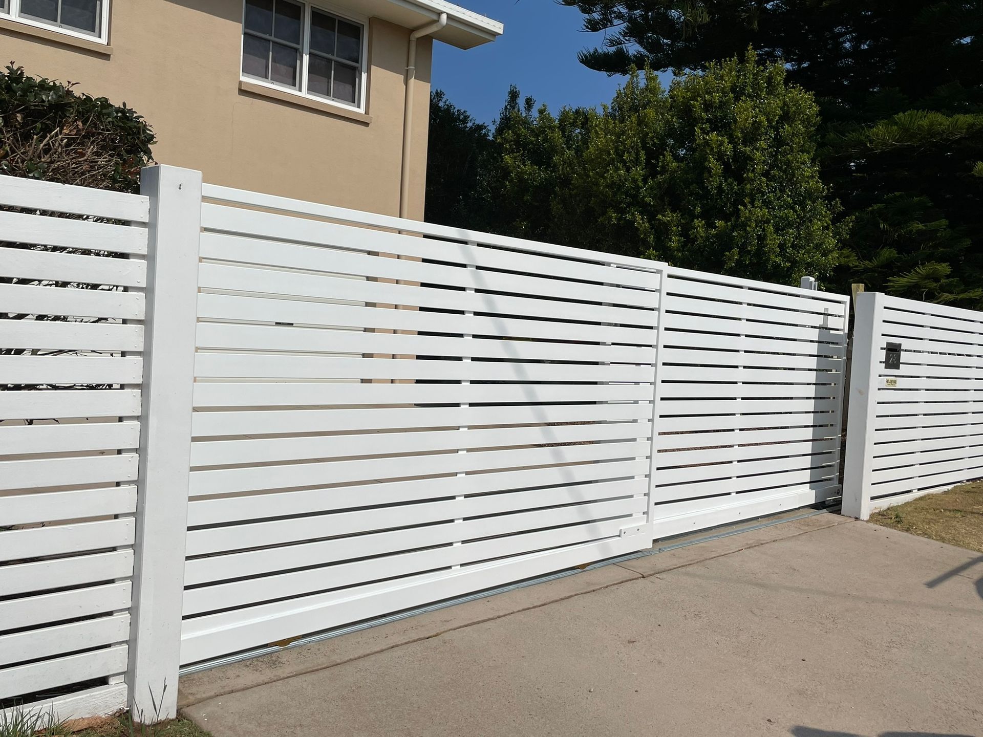 A white fence with a sliding gate in front of a house.