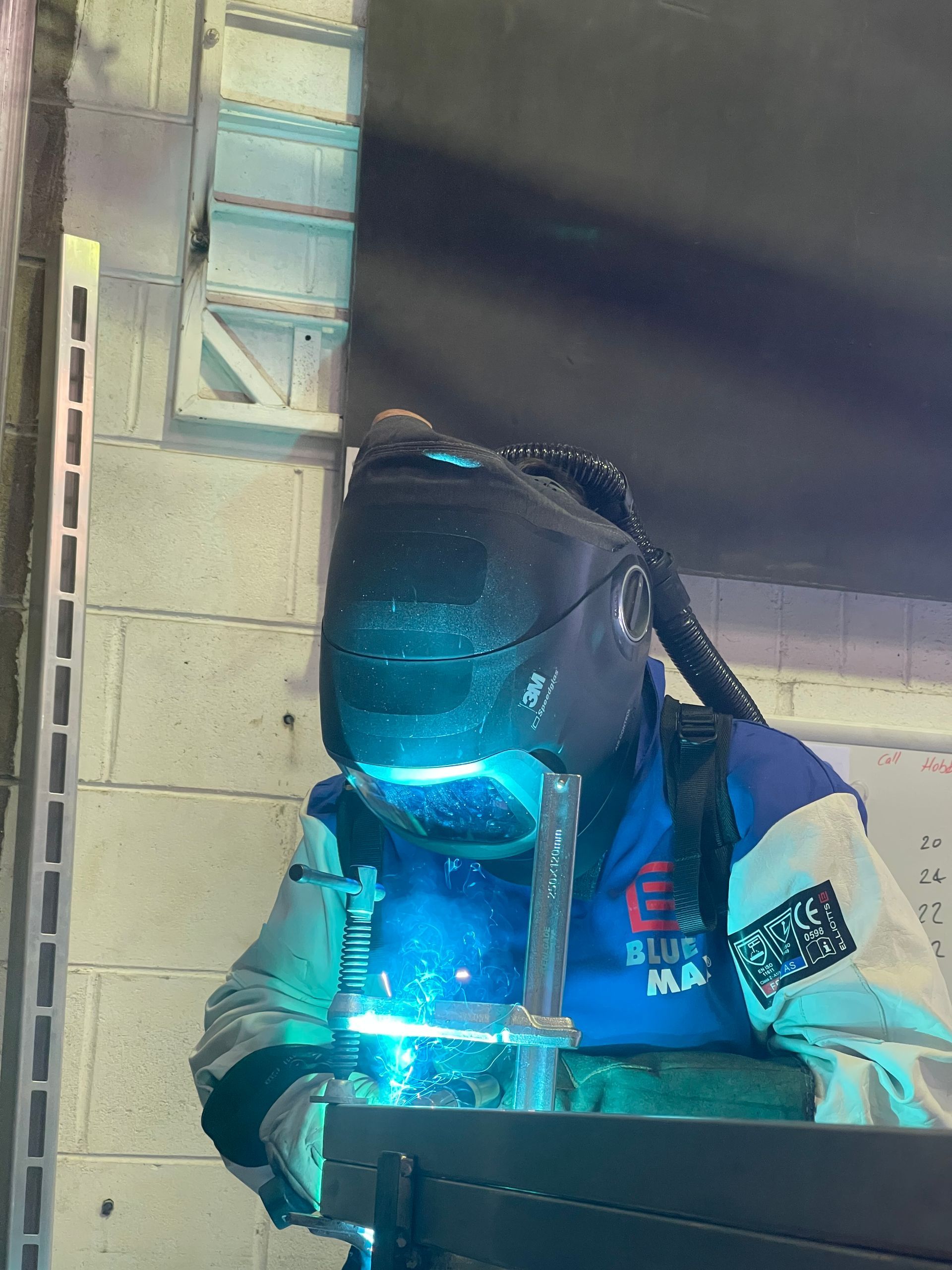 A person wearing a welding mask is welding a custom metal gate.
