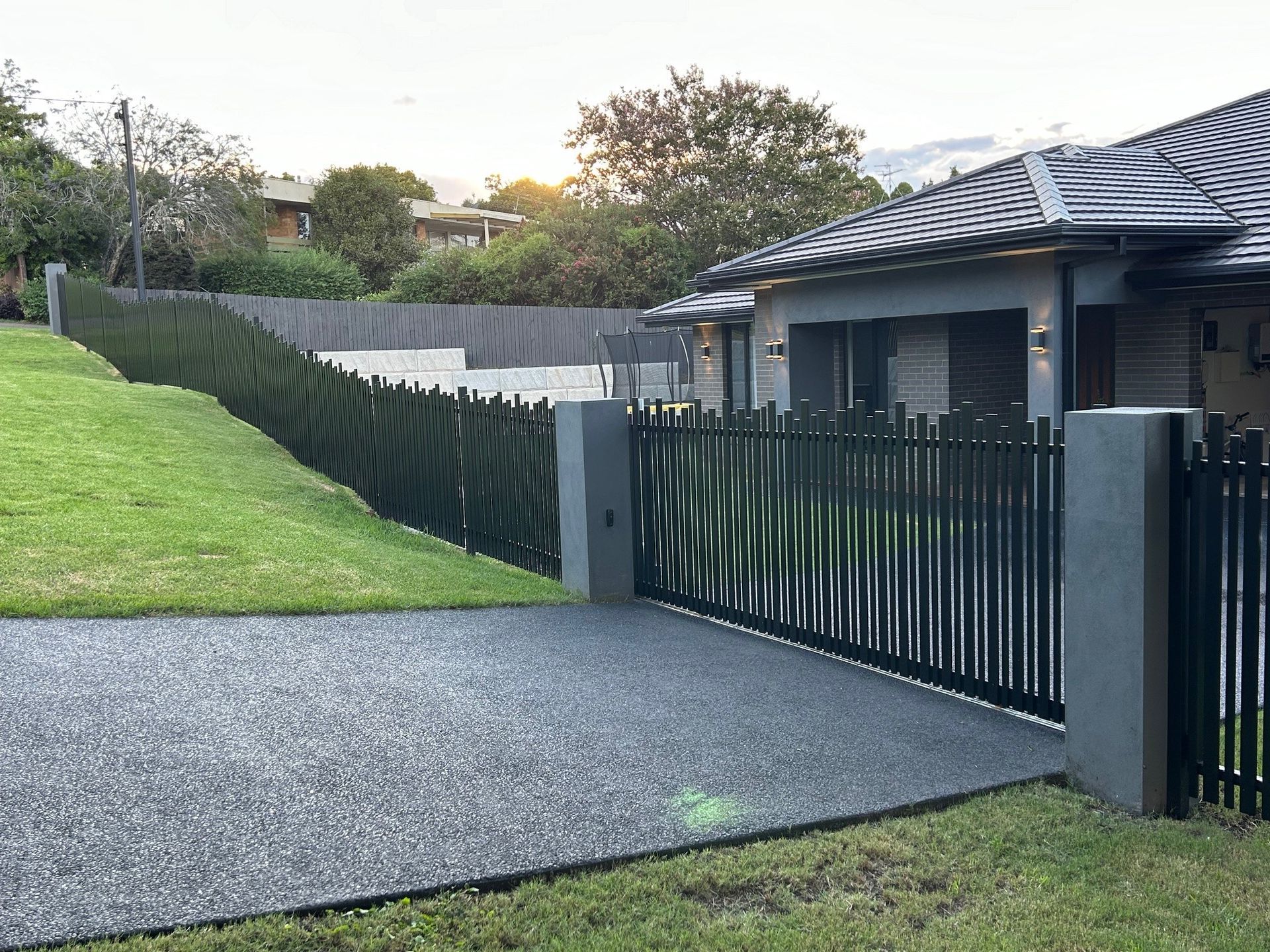 A black fence surrounds a driveway leading to a house.
