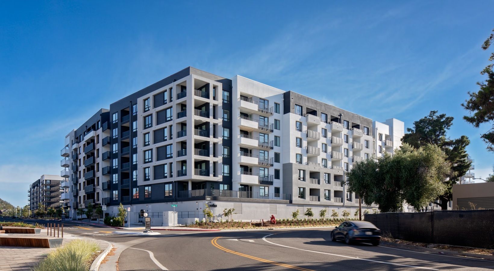 Exterior view of a modern, multi-story apartment building along a curved street with landscaping at Sofia.