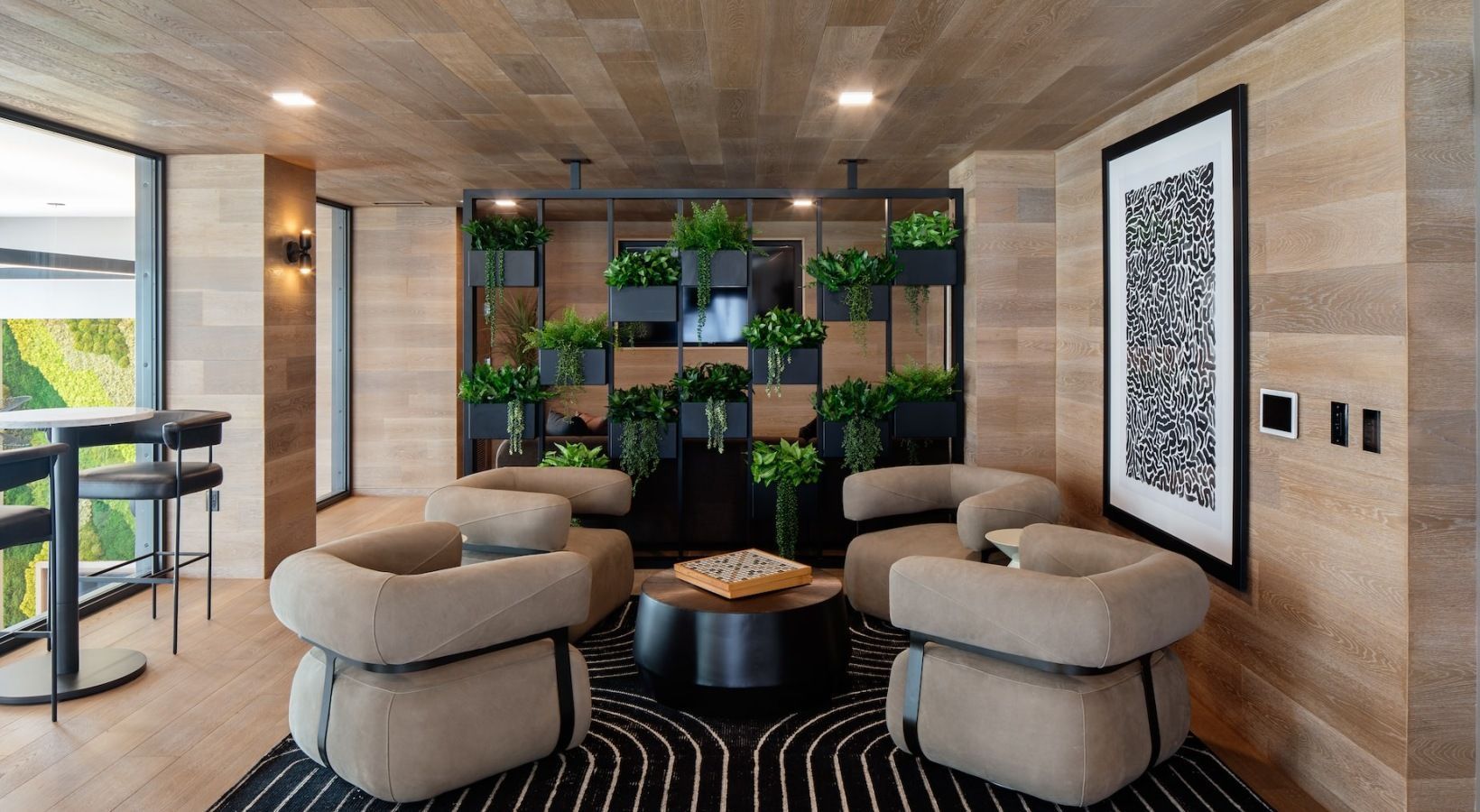 Modern apartment community lounge with beige curved chairs, a plant divider, and wall art at Sofia, offers apartments for rent in Santa Clara, CA.