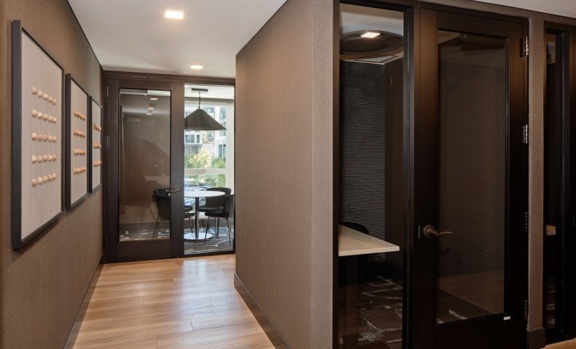 Interior hallway of a modern apartment community with dark wood doors and a glass-walled conference room at the end at Sofia, offers apartments in Santa Clara.